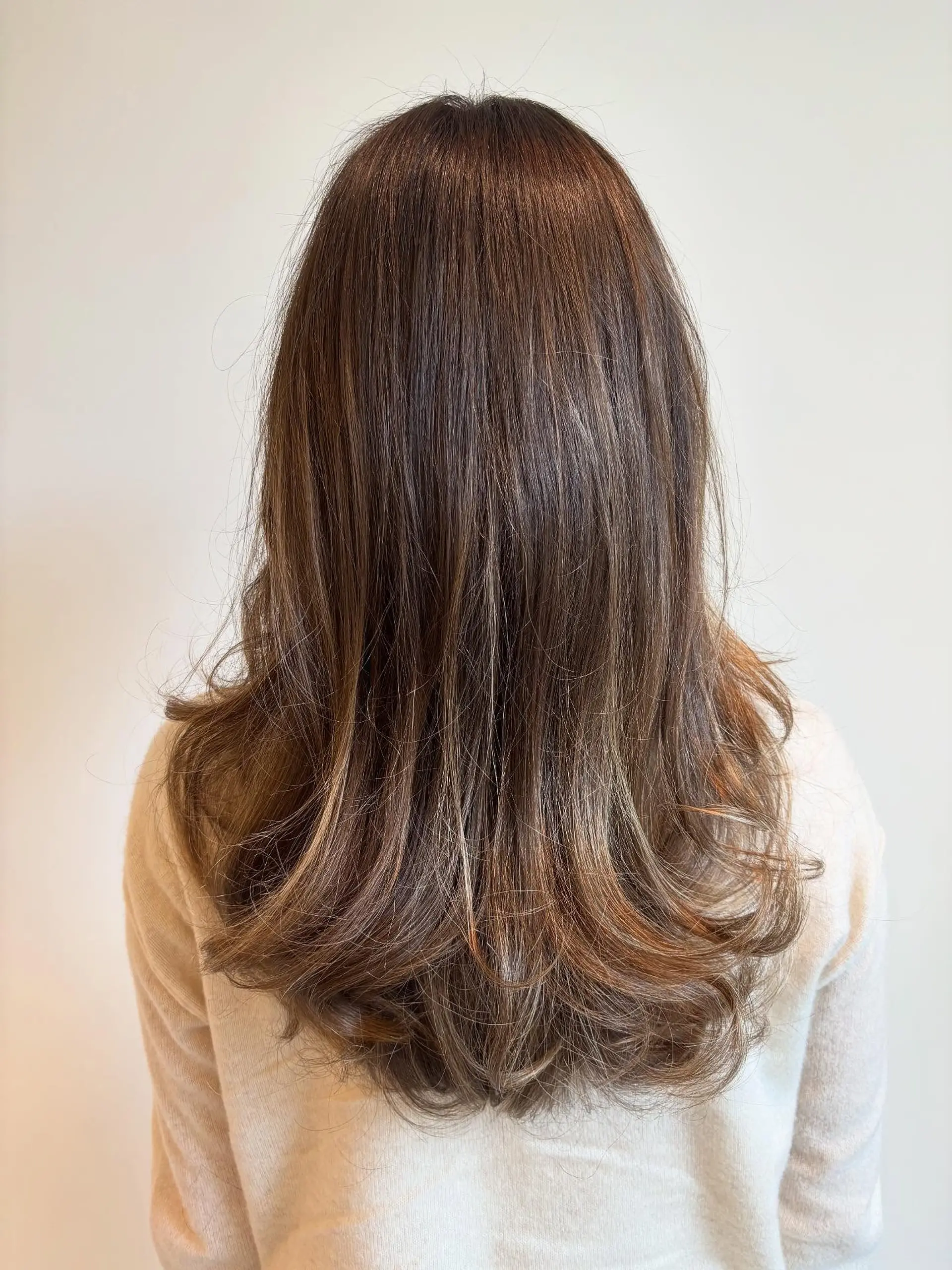 Long layered brunette hair with subtle golden balayage highlights, styled with soft outward flips at the ends. 1