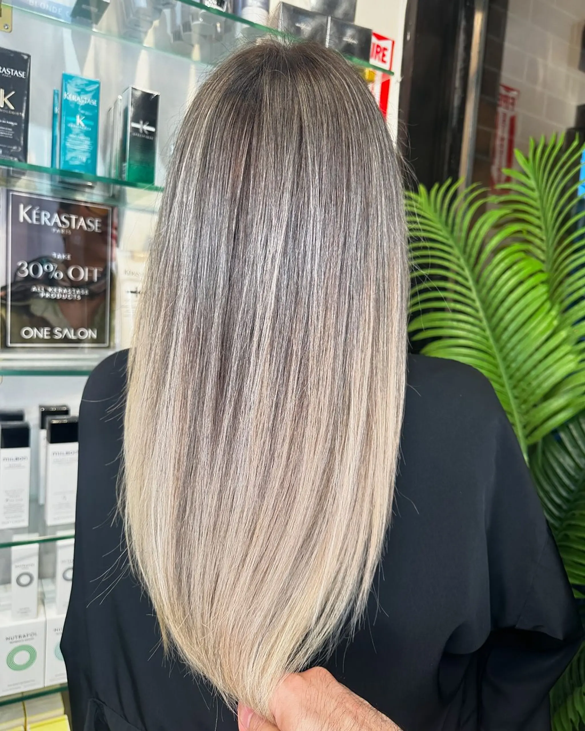 A sleek, straight hairstyle that transitions from silver at the roots to ash blonde and platinum at the tips, featuring long length and a cool toned, multidimensional color effect.