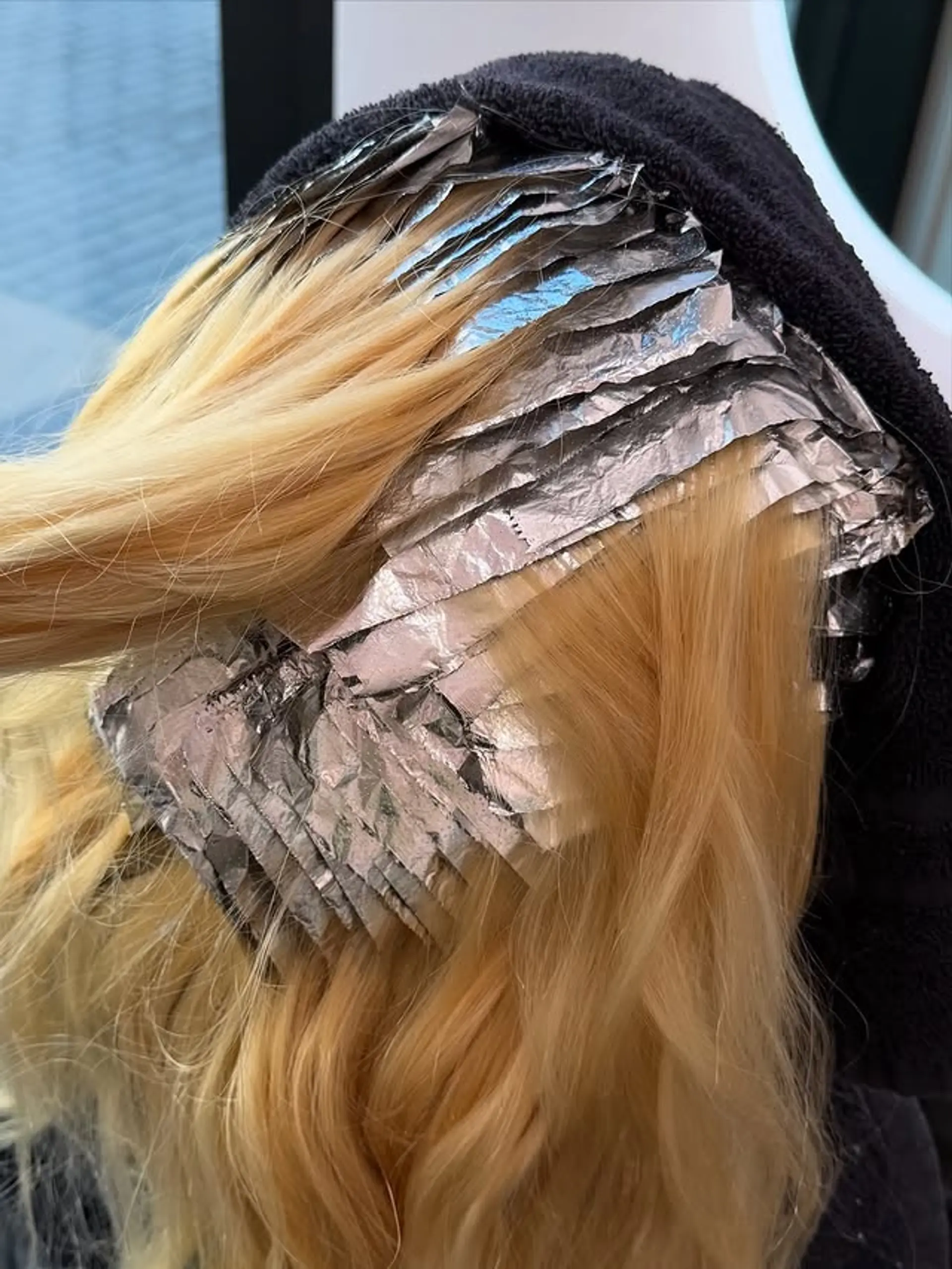 A full head global bleach retouch, utilizing foils to meticulously lighten new growth and enhance existing blonde, resulting in a bright, uniform, and radiant blonde hair color. 1