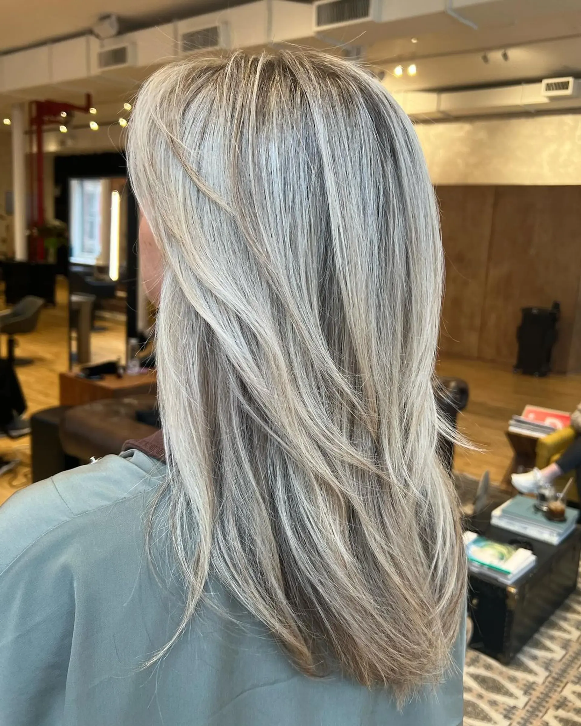 Long, straight hair with sophisticated layers and a blend of blonde and platinum hues, enhanced by subtle highlights and complemented by a middle part. 1