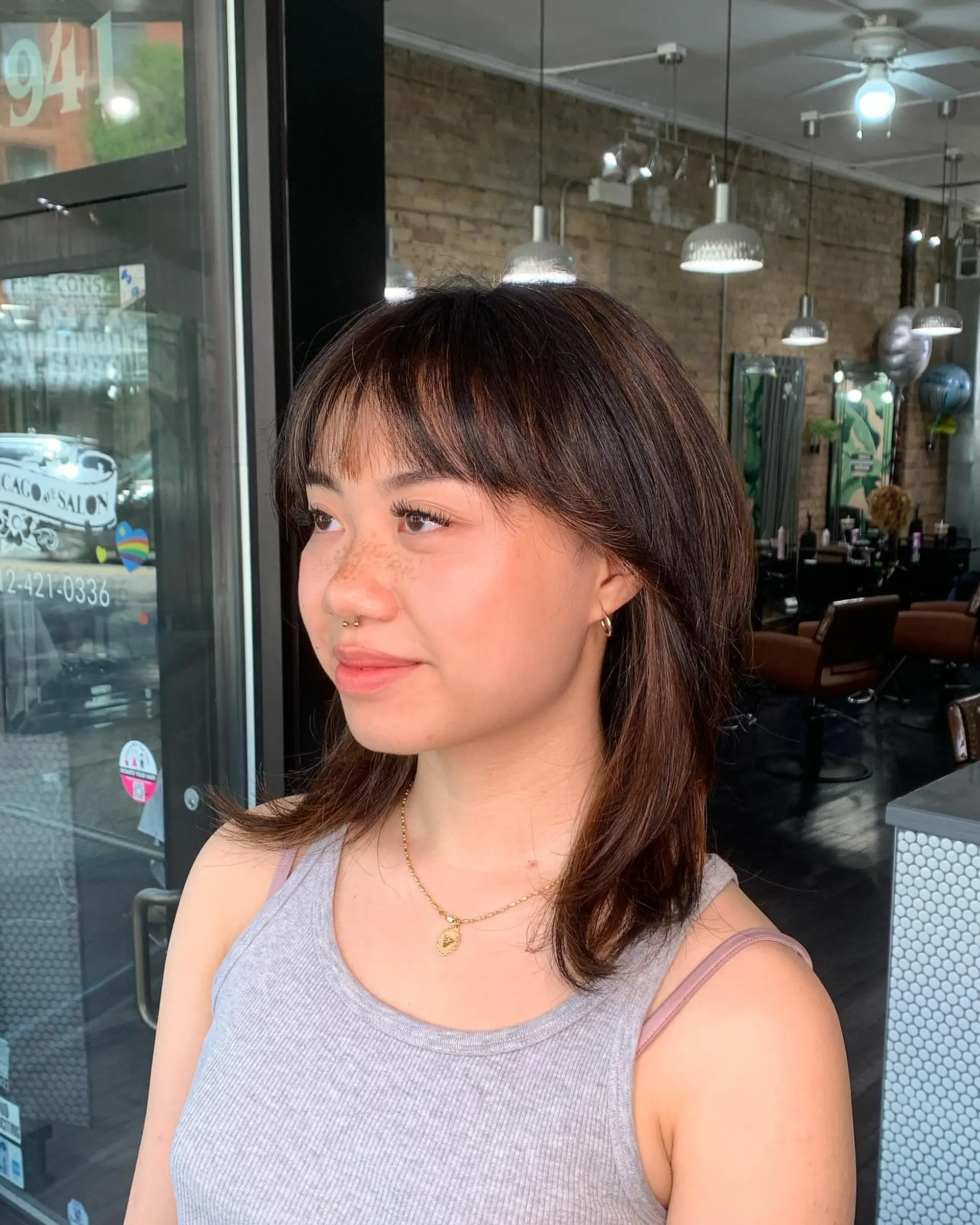 Medium-length layered brunette hairstyle featuring wispy brow-skimming bangs and subtle warm highlights. 1