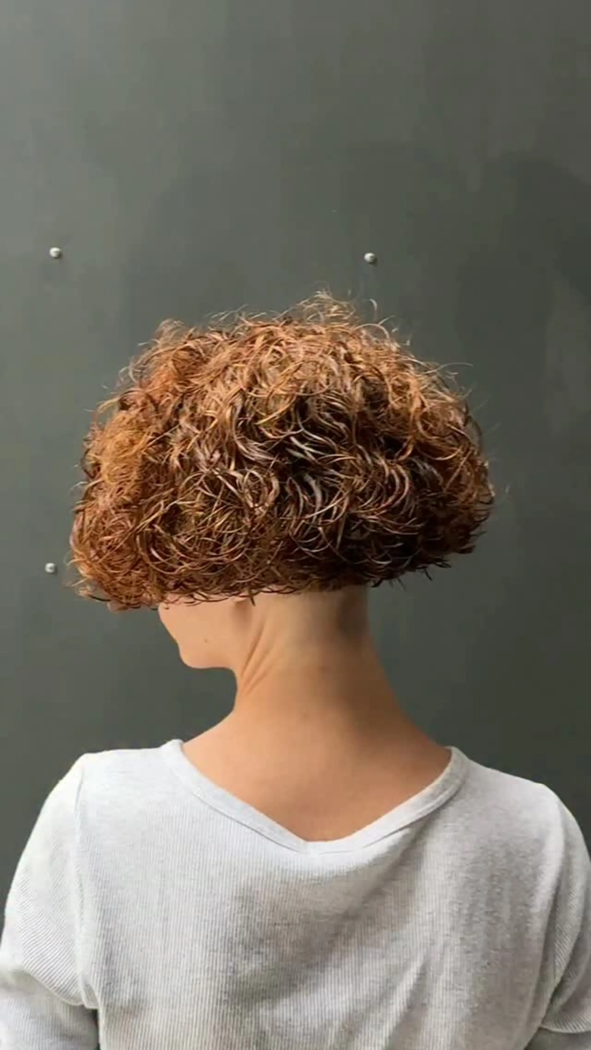 A structured, voluminous short curly bob cut cleanly above the nape of the neck. 1
