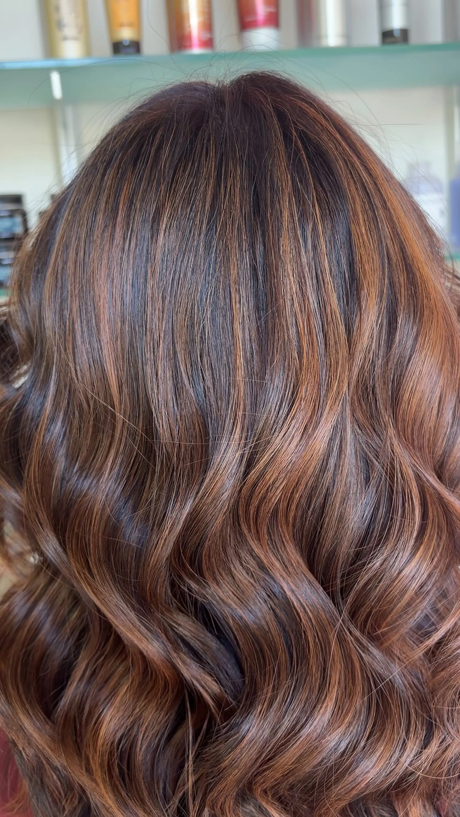 Medium-length dimensional brunette hair styled in soft, loose waves with warm caramel highlights. 1