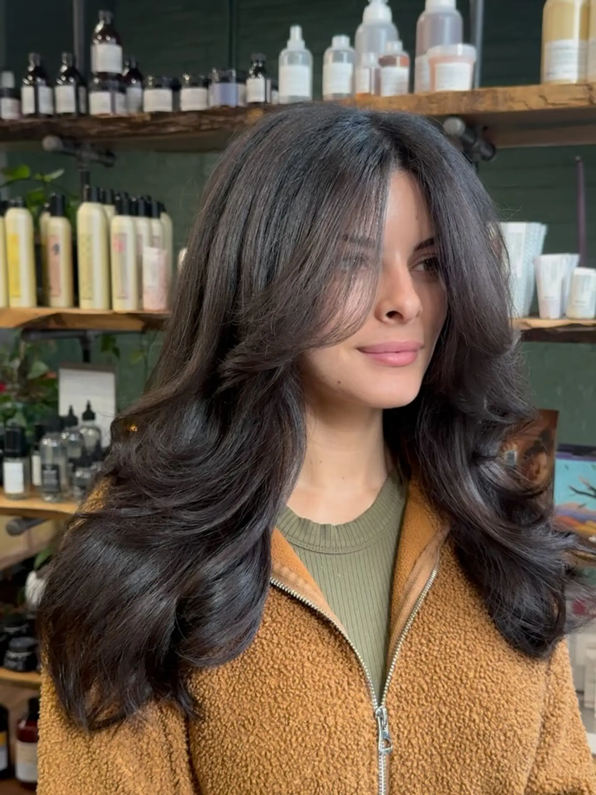 A rich espresso-toned long haircut styled with voluminous, bouncy layers and soft face-framing curtain bangs. 1