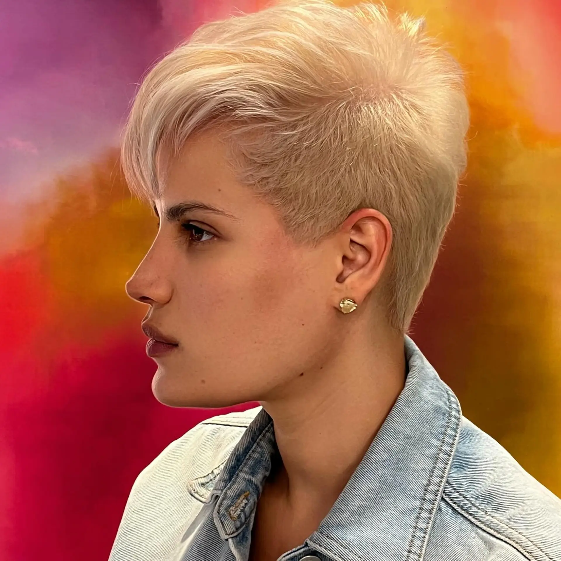 A textured platinum blonde pixie cut featuring tapered sides and soft, feathered fringe. 1