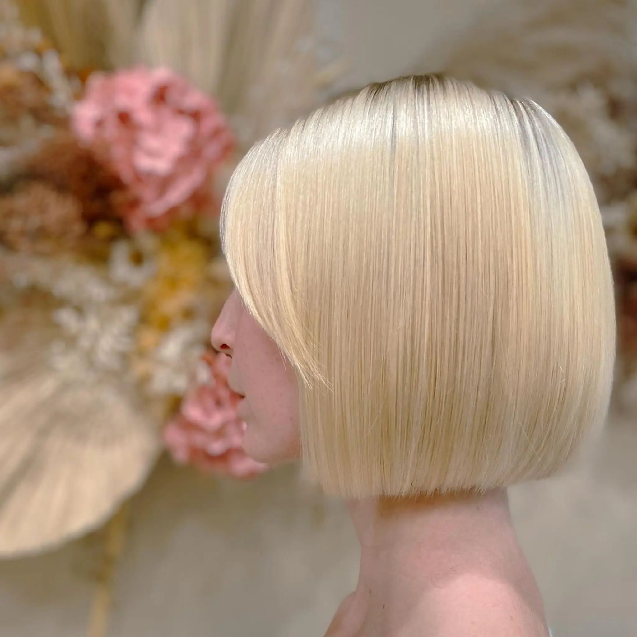 A sleek, straight short bob with a platinum blonde hue, characterized by a blunt cut and precision edges, creating a symmetrical, ear-length appearance with a glossy finish.