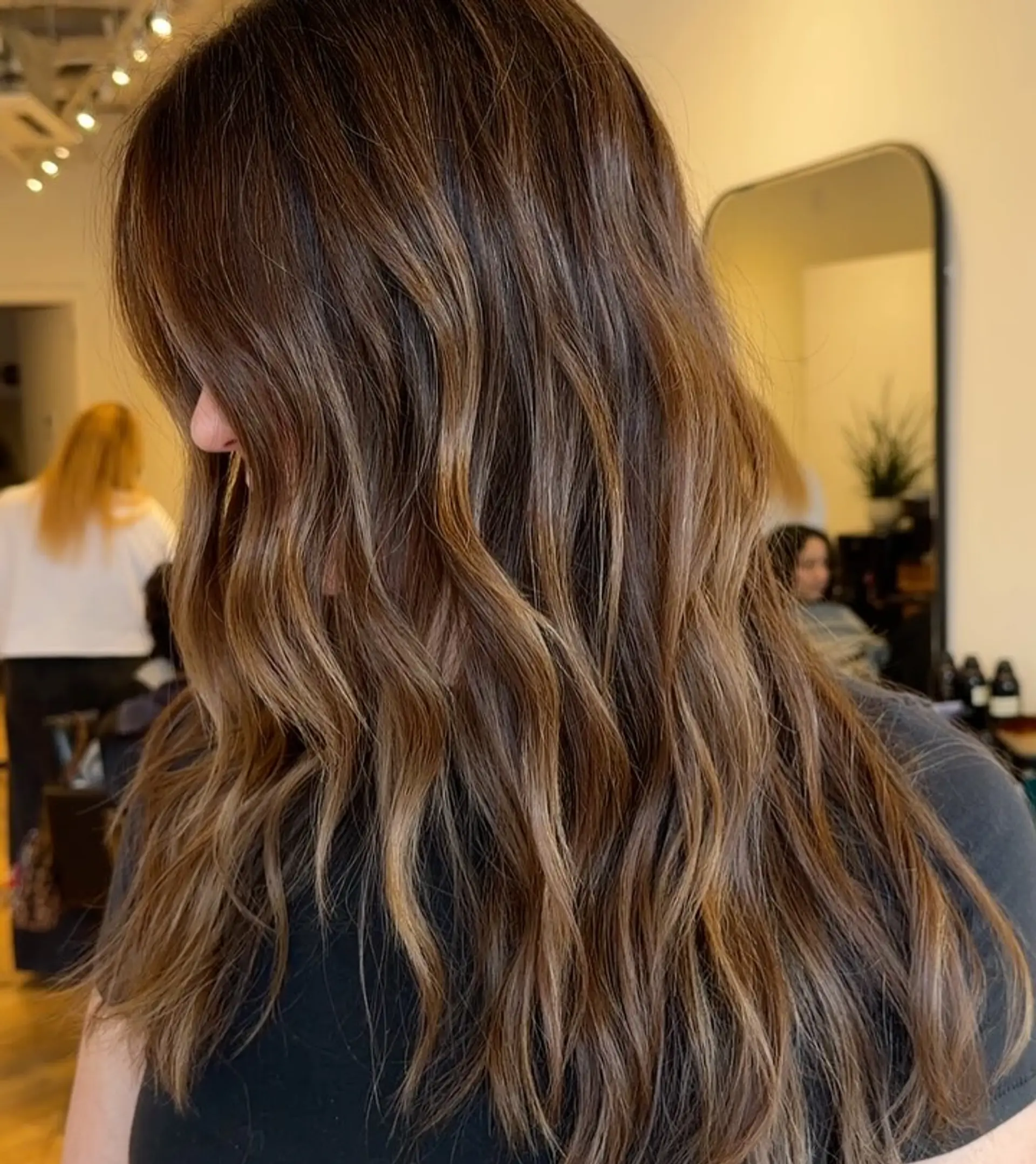 Long, tousled wavy brunette hair enhanced with fine caramel highlights throughout. 1