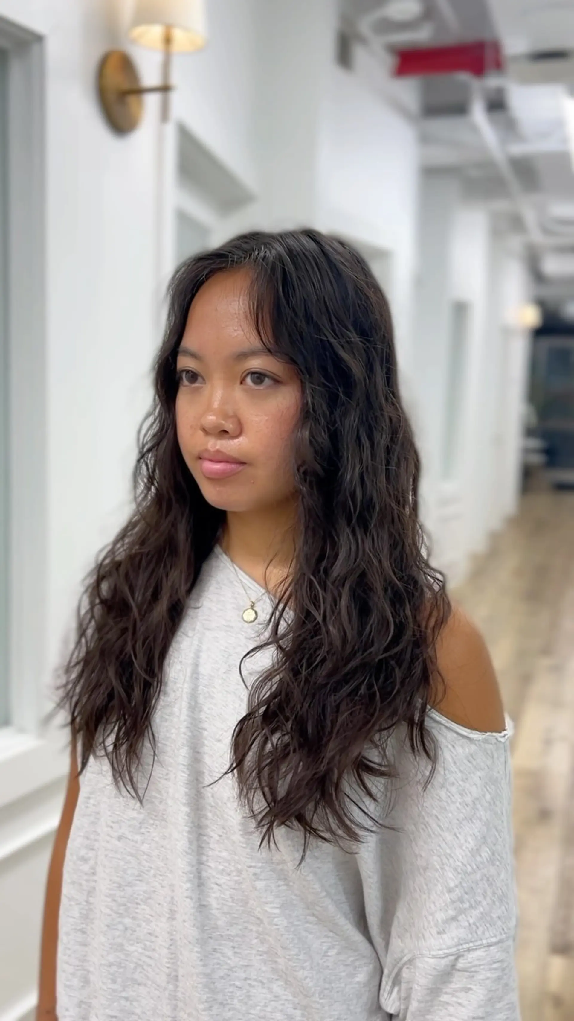 Long dark hair styled into effortless, soft beachy waves created with a digital perm, complete with center-parted face-framing fringe. 1
