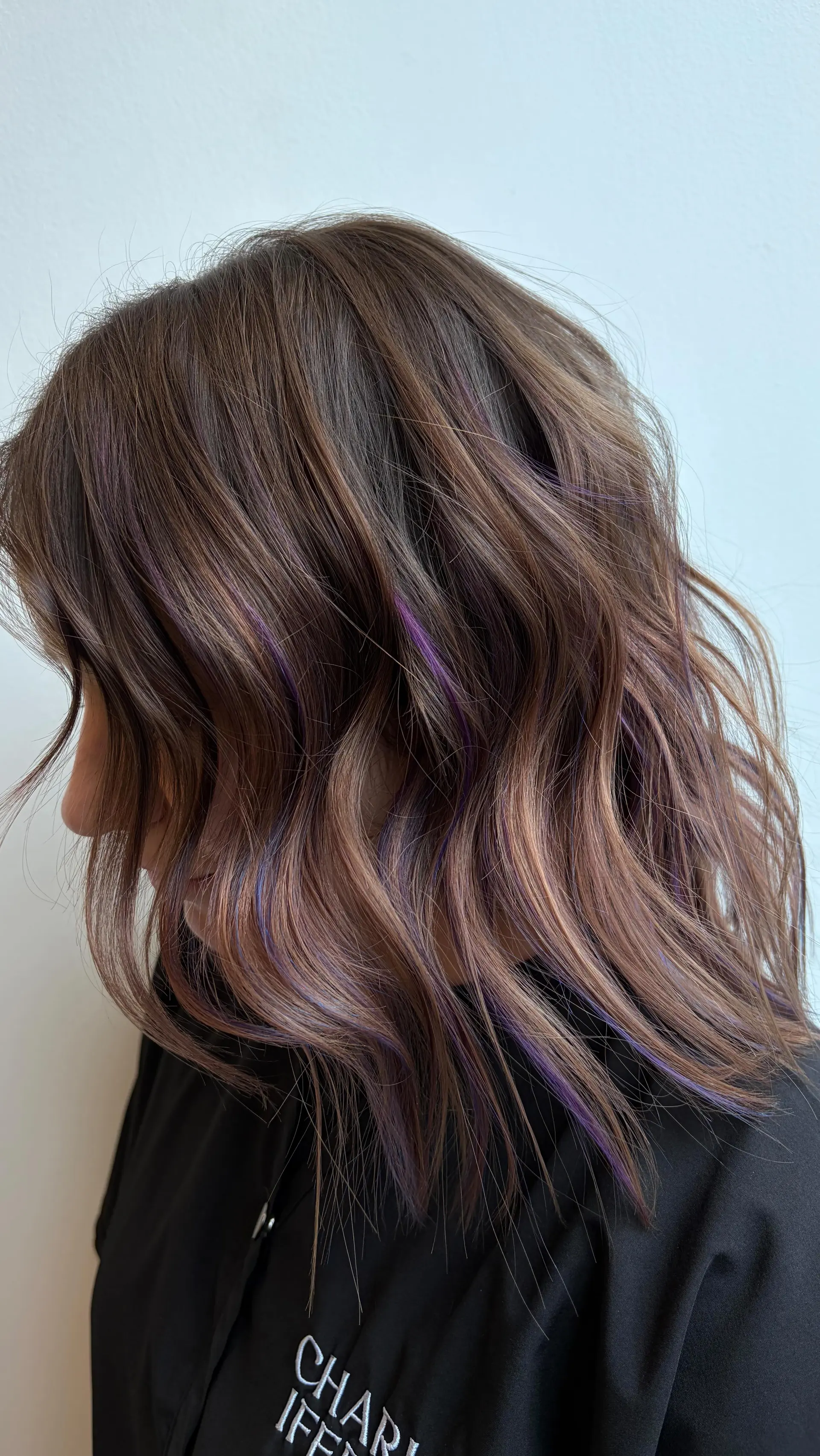 A medium-length textured lob with loose dimensional waves featuring subtle purple peekaboo highlights under a cool mushroom brown base. 1