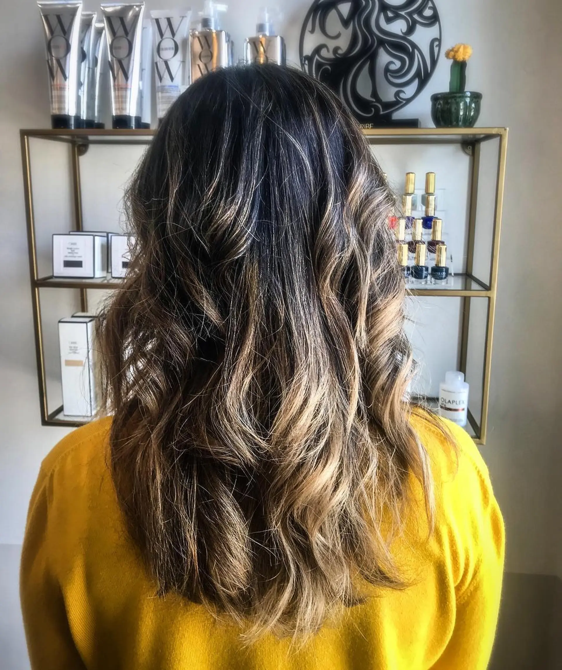Long dark hair enhanced with warm golden highlights and styled in soft, cascading waves. 1