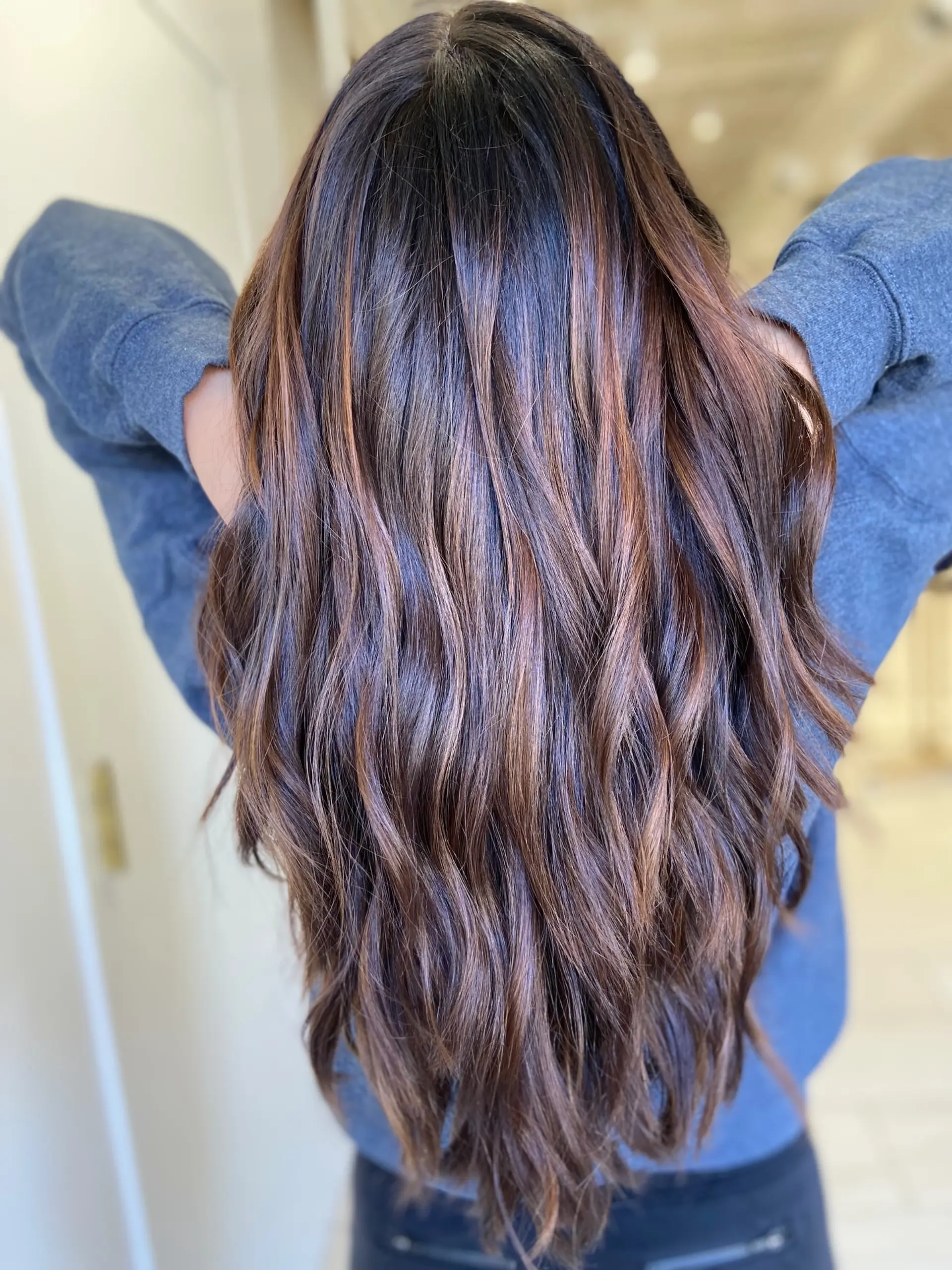 Long dimensional brunette hair styled in loose, textured waves with warm caramel highlights woven throughout. 1