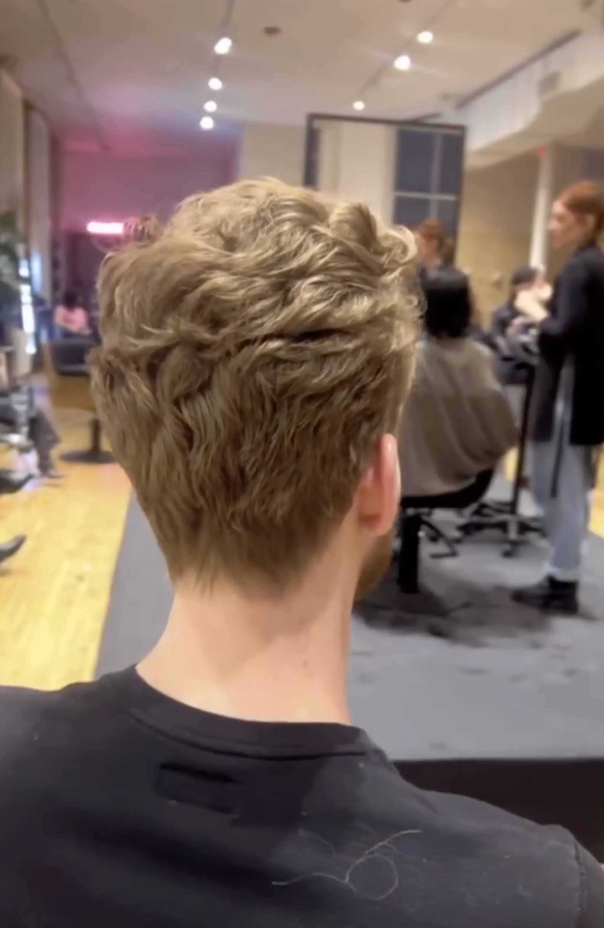 A short, tapered, and textured golden brown wavy hairstyle with layers creating a tousled yet polished appearance.