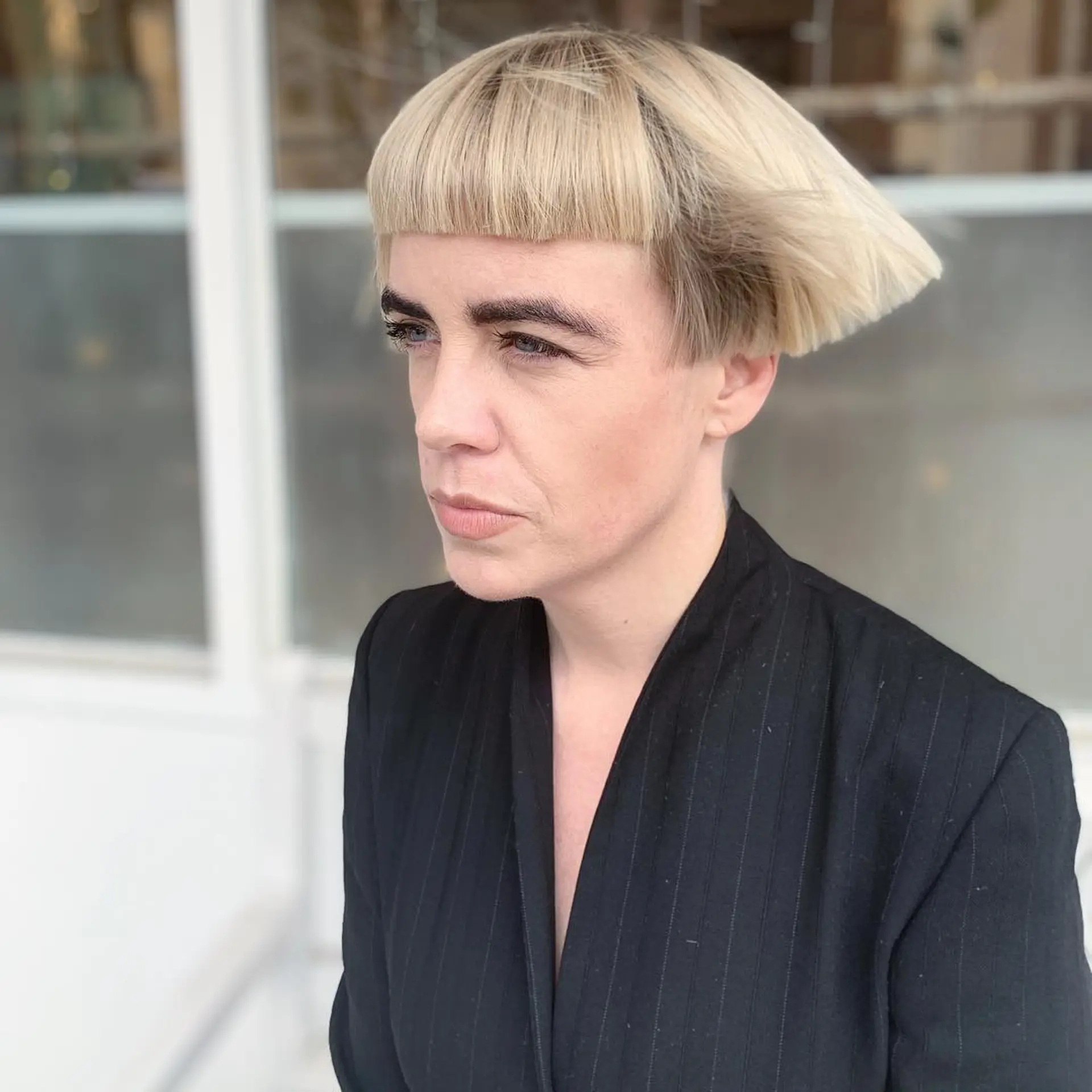 A sleek, blonde bowl cut with a straight texture, short length, and a sharp undercut at the nape for a modern, uniform appearance. 2