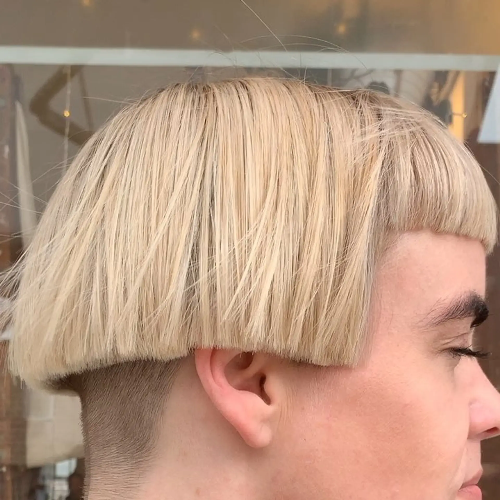 A sleek, blonde bowl cut with a straight texture, short length, and a sharp undercut at the nape for a modern, uniform appearance. 3