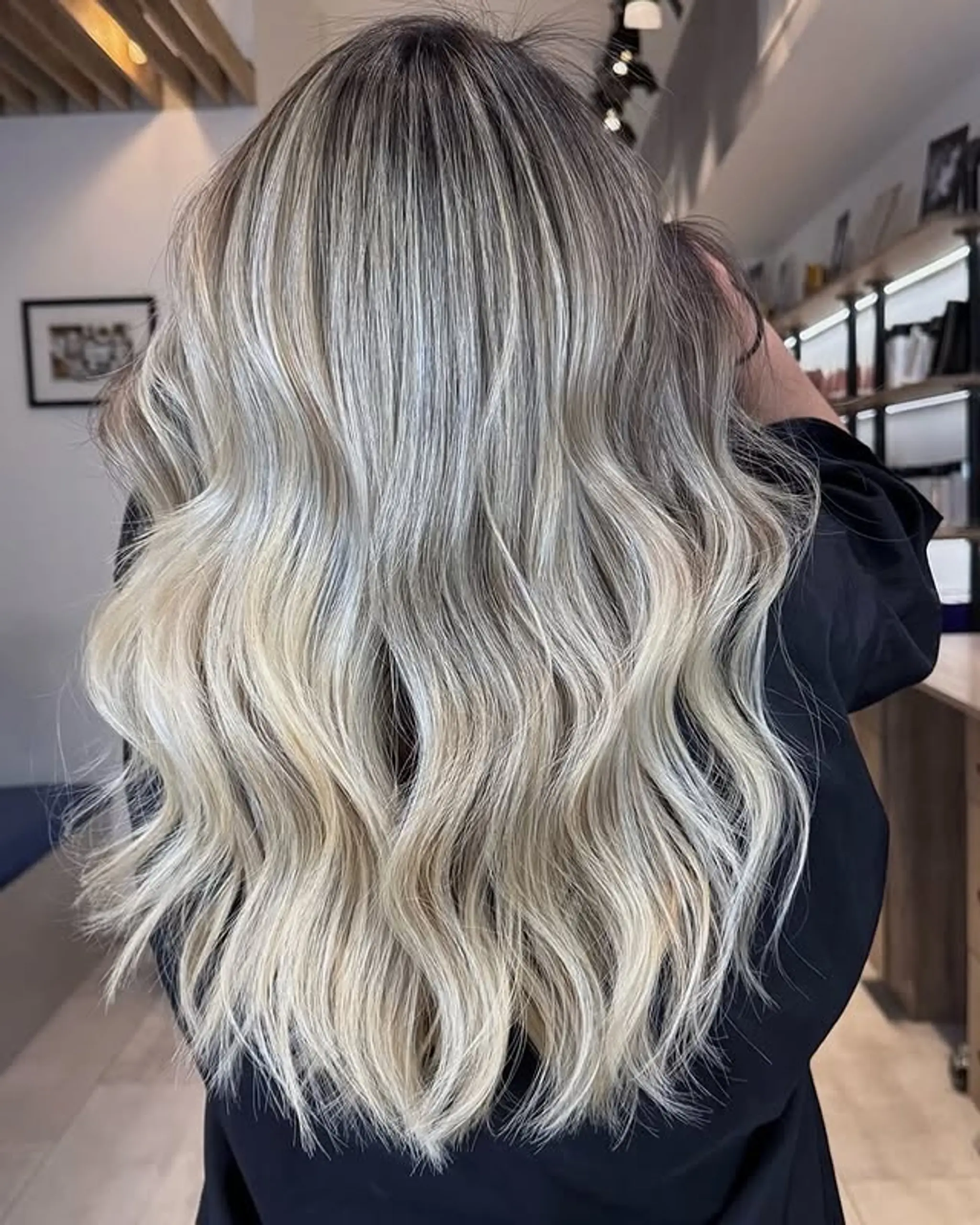 Long, effortless waves with a platinum blonde balayage that transitions from dark roots to ash blonde highlights.