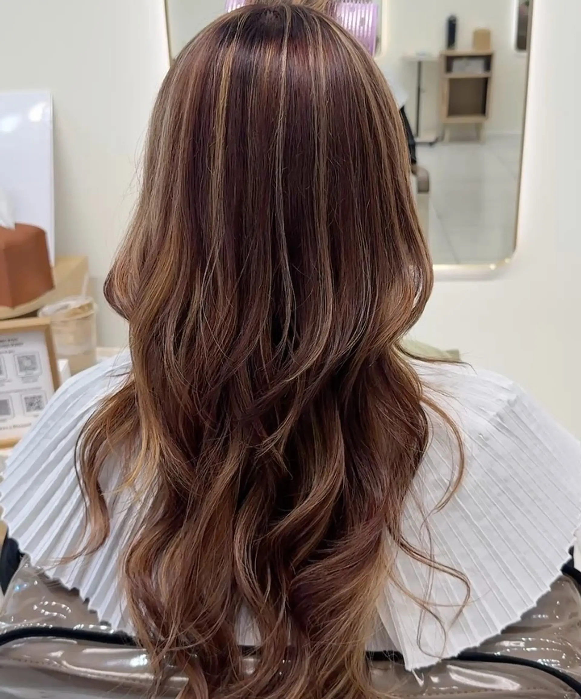 Long warm brown hair styled in soft cascading waves with dimensional caramel highlights. 1