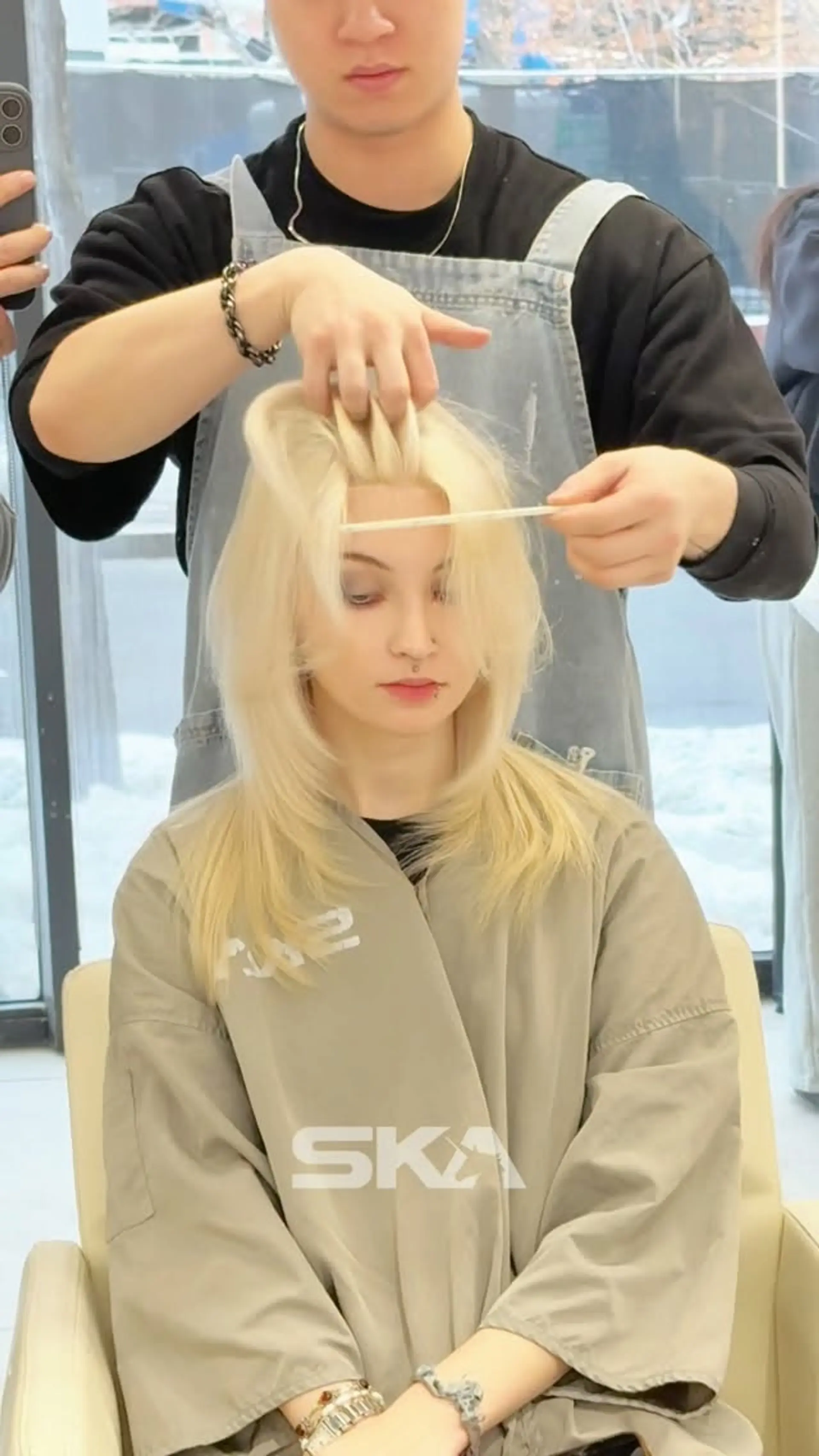 Medium-length icy platinum blonde haircut featuring soft feathered layers and face-framing curtain bangs. 1