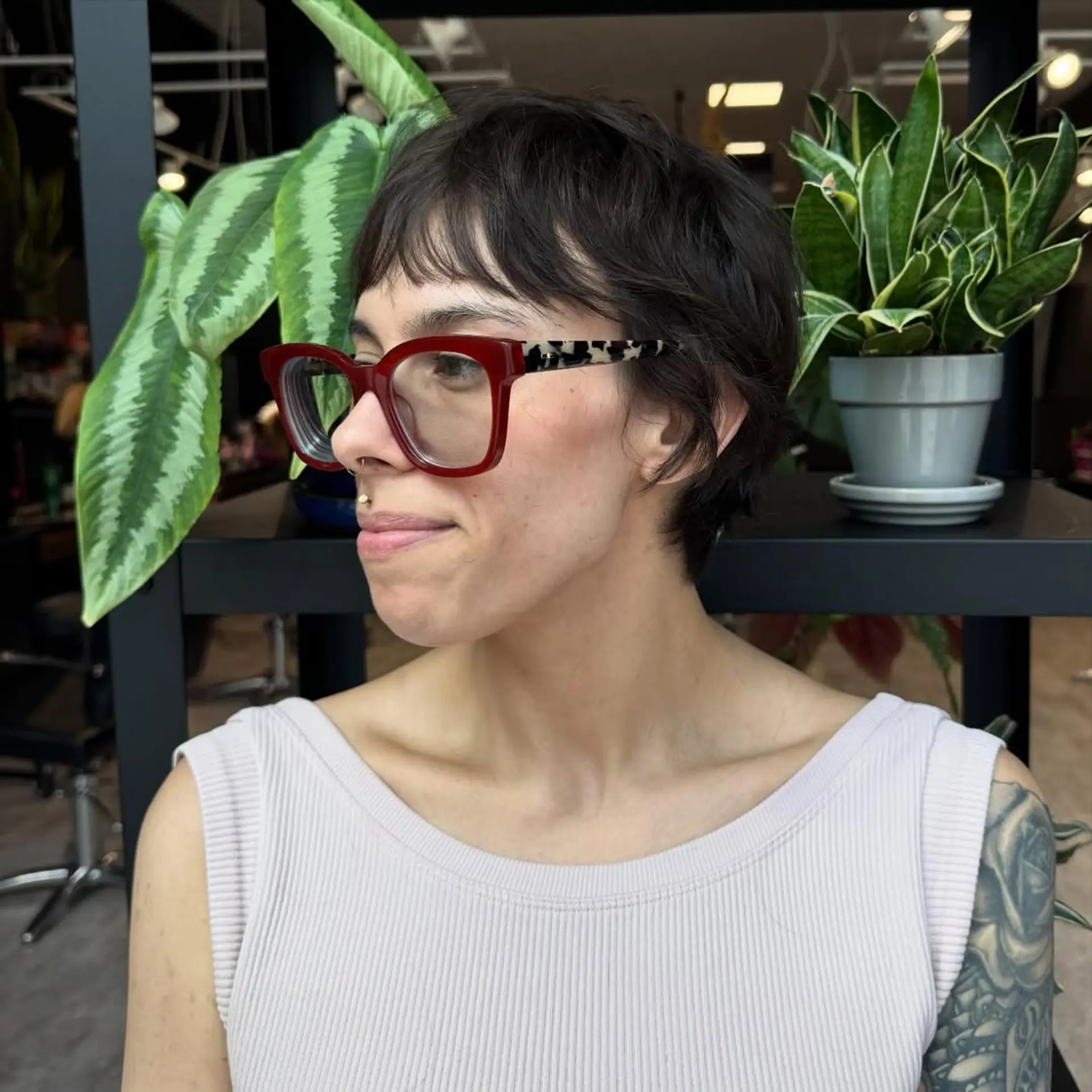A very short, dark brown choppy pixie cut with textured layers and a short, wispy fringe. The style is designed to enhance natural wavy texture, providing a modern and slightly messy aesthetic. 1
