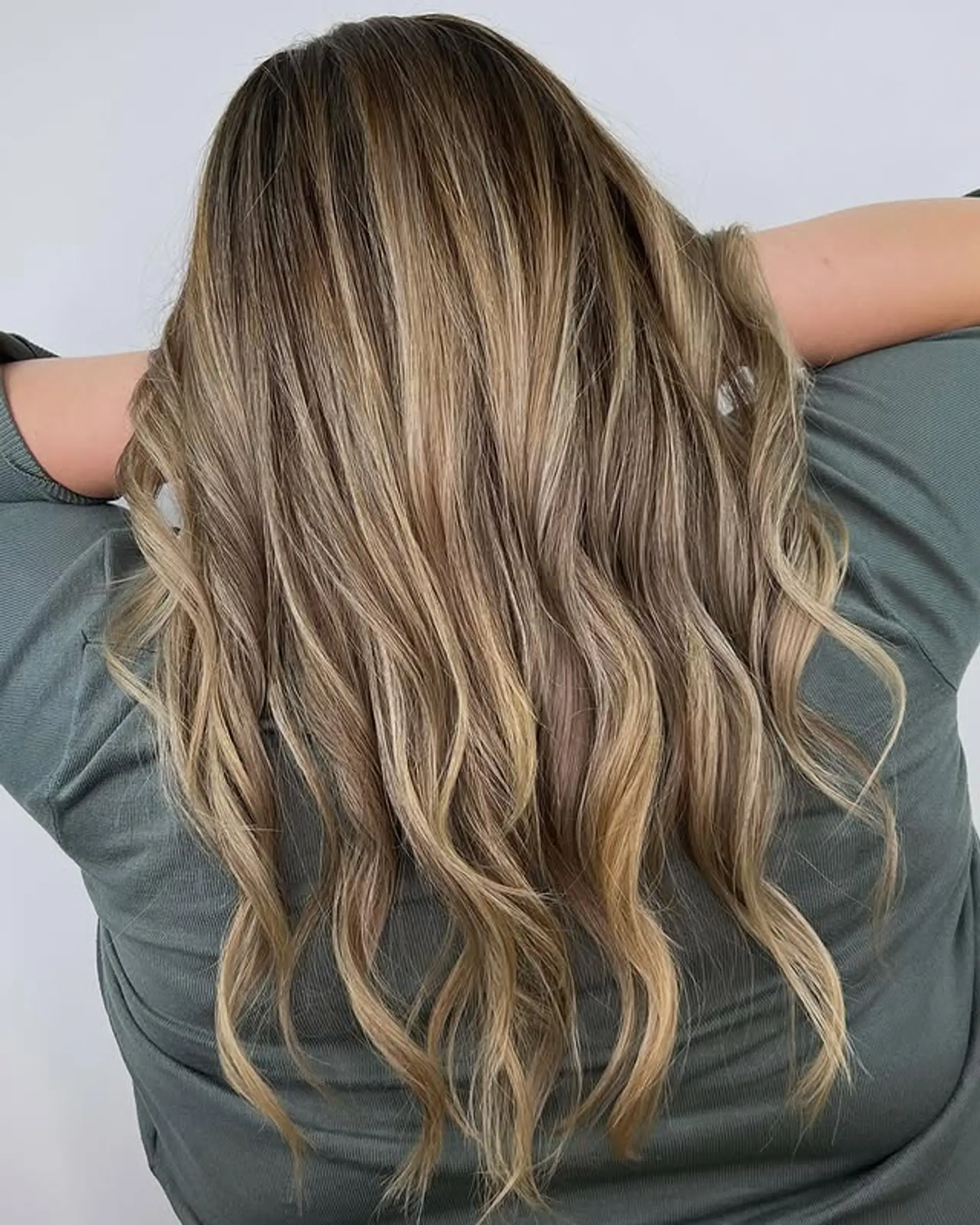 Long, flowing wavy hair with a caramel blonde balayage that creates a blended, sun-kissed effect. 1