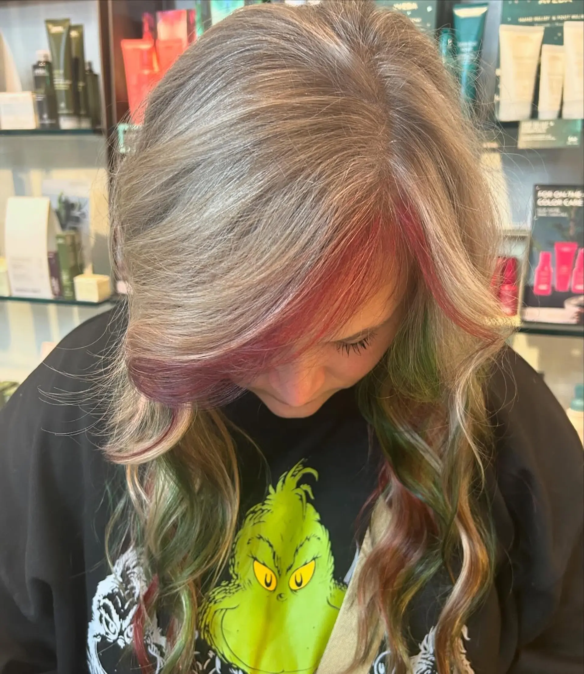 Long ash blonde hair with soft waves featuring vibrant red and green holiday peekaboo highlights framing the face. 1
