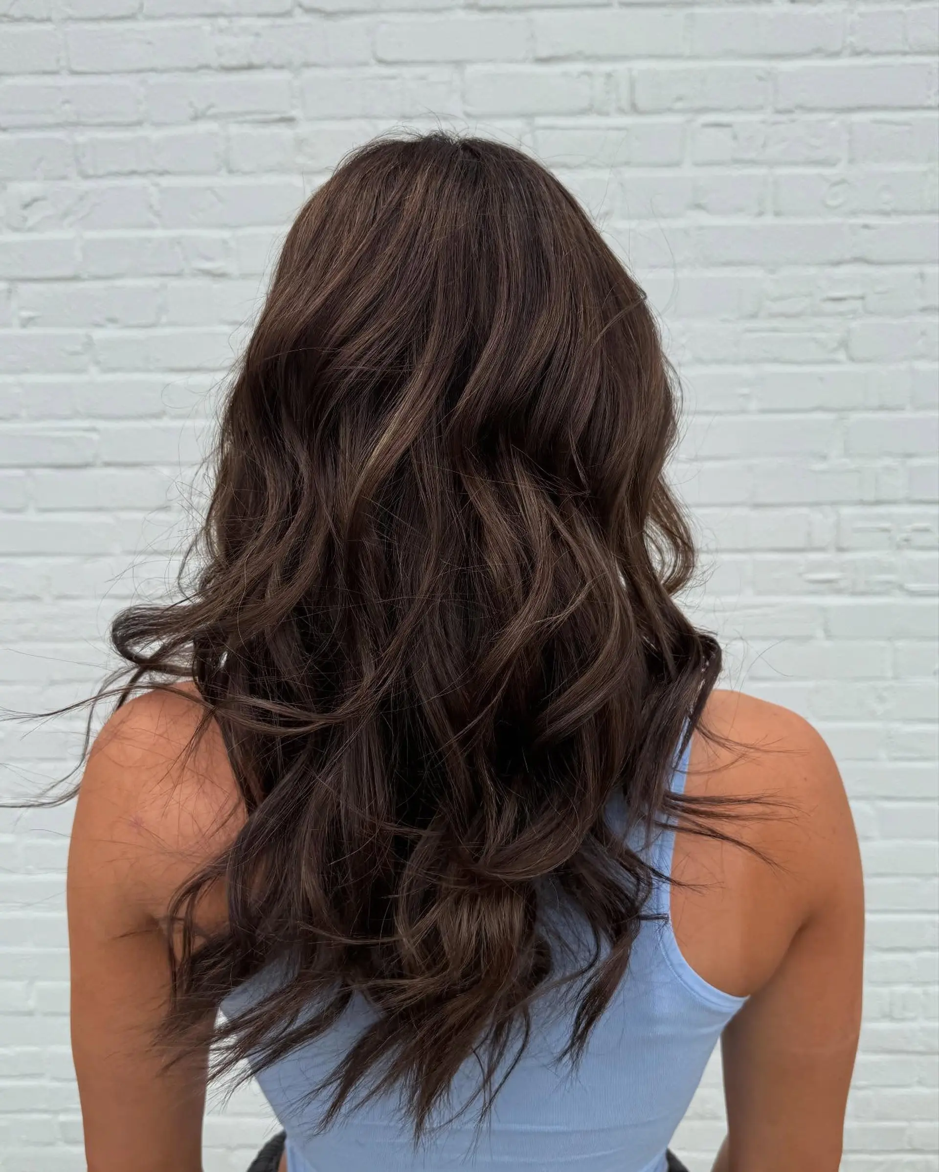 Long chocolate brown hair styled into soft, flowing textured waves with subtle dimensional tones. 1