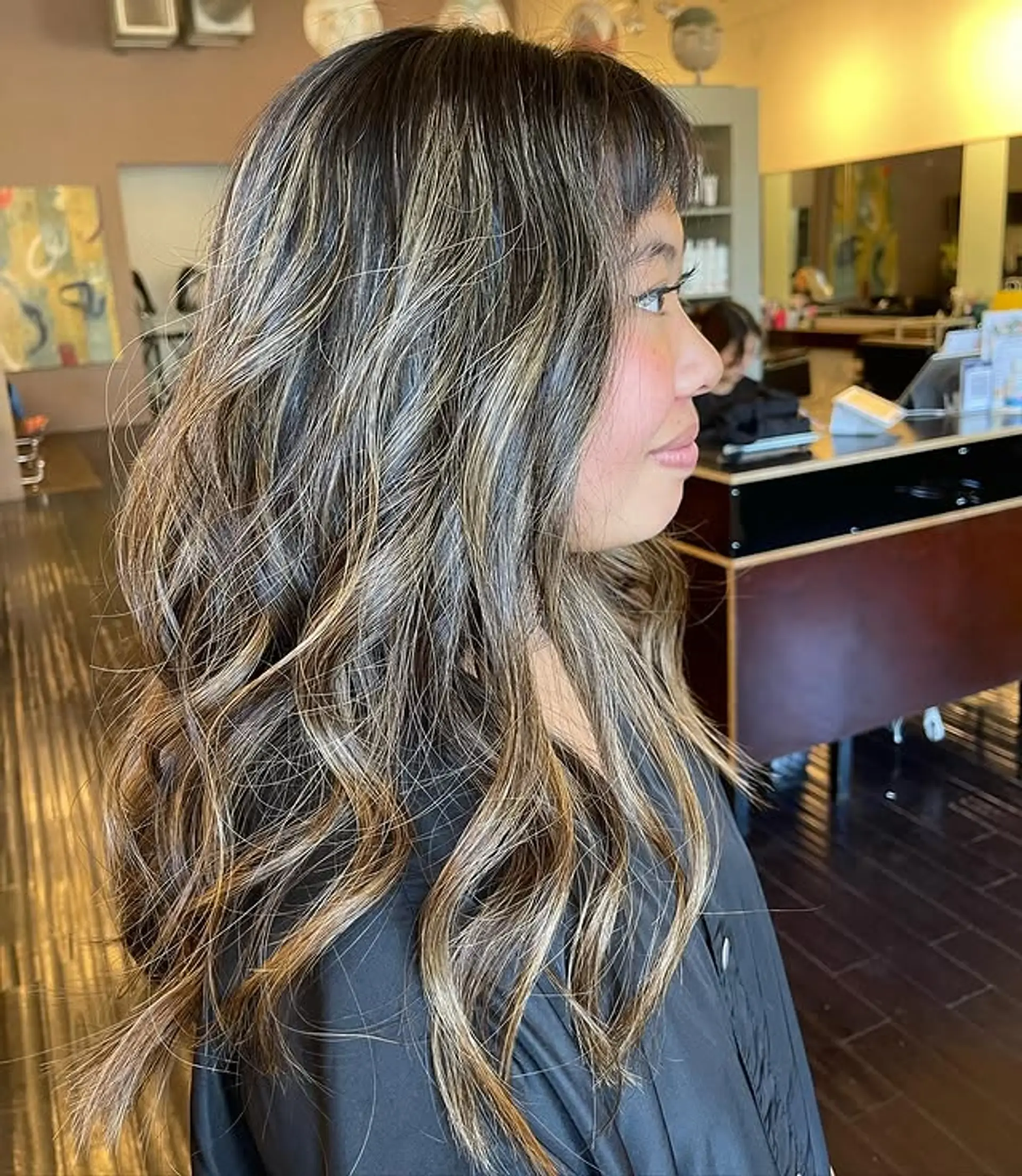 A wavy, medium-length hairstyle featuring balayage highlights and face-framing bangs. 1