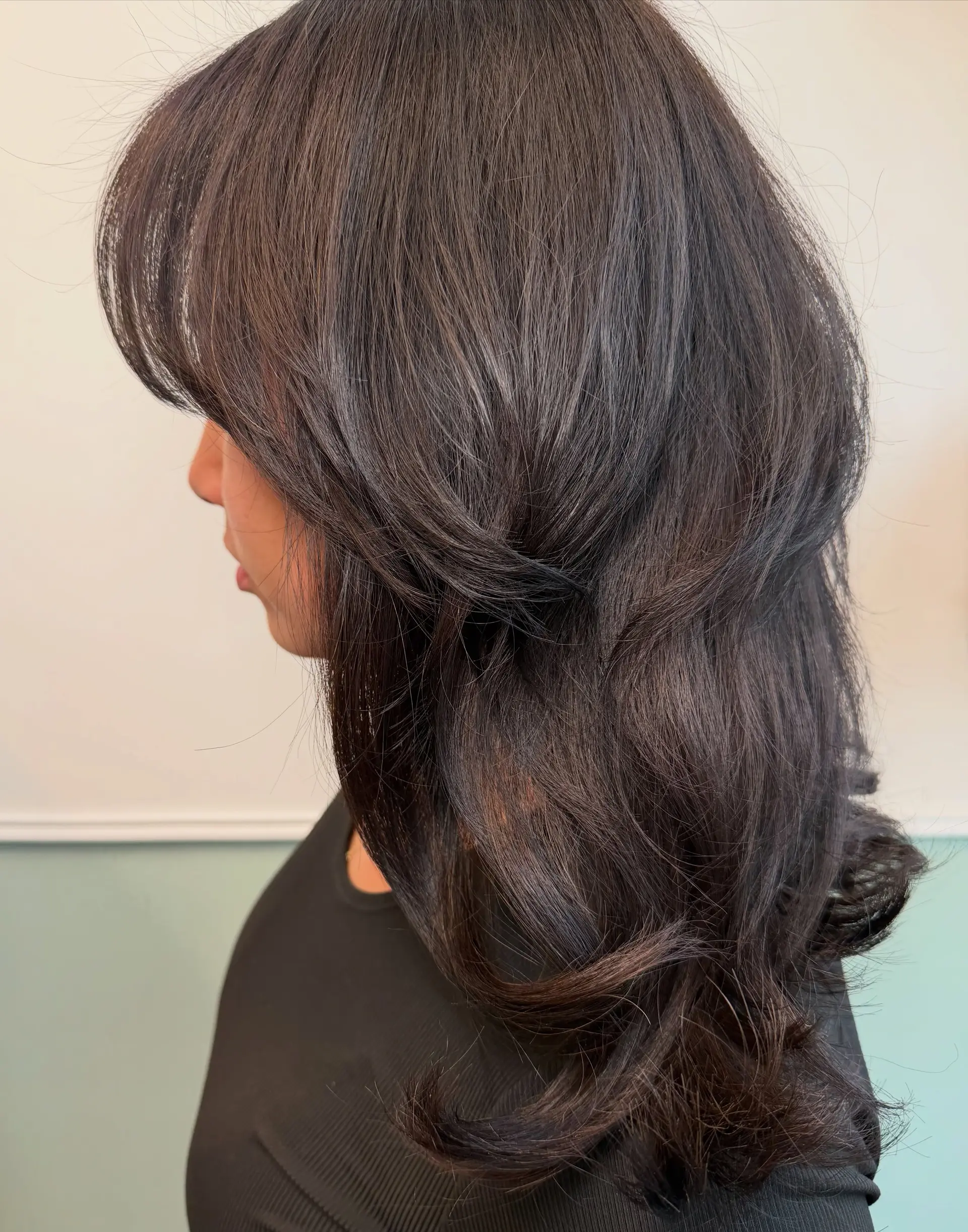 A rich dark brunette layered haircut featuring sweeping face-framing curtain layers and soft, dimensional waves. Current Haircut option: $140 before tax. Haircut and included finish only; color is not included. 1