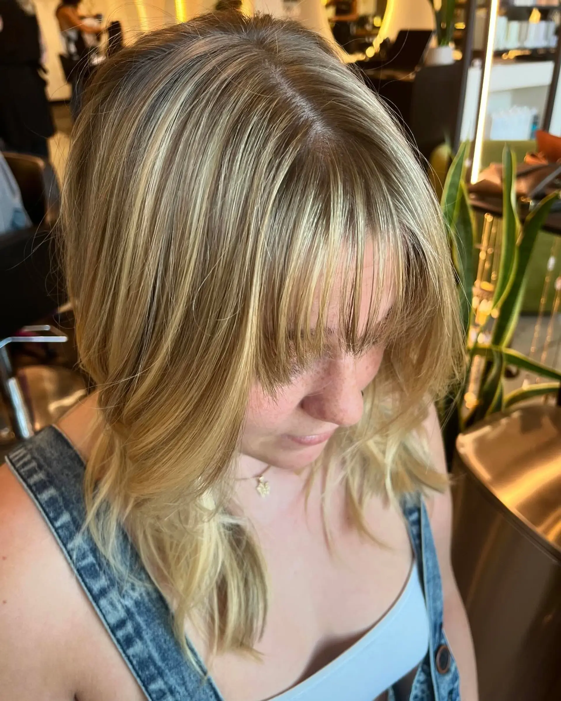 Medium-length dimensional blonde hair with finely blended highlights and textured, wispy fringe bangs. 1