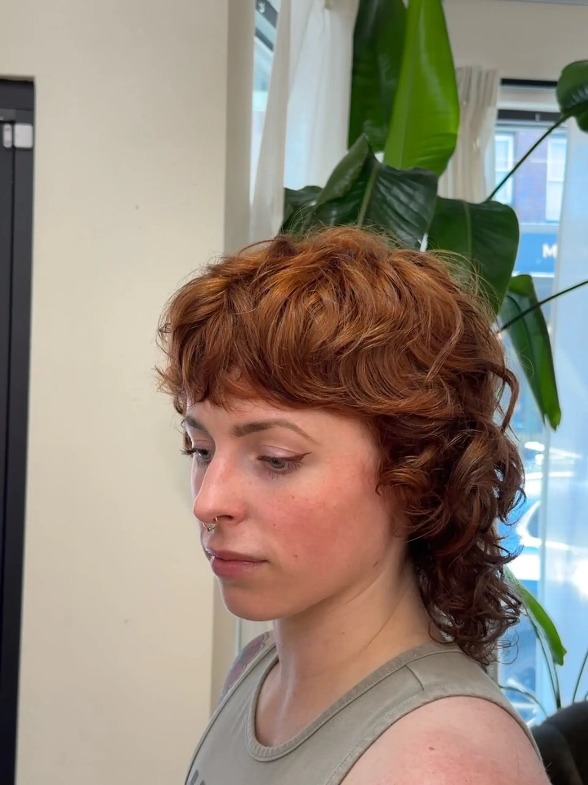A textured wavy modern mullet cut in a vibrant copper red tone with soft, tousled bangs. 1