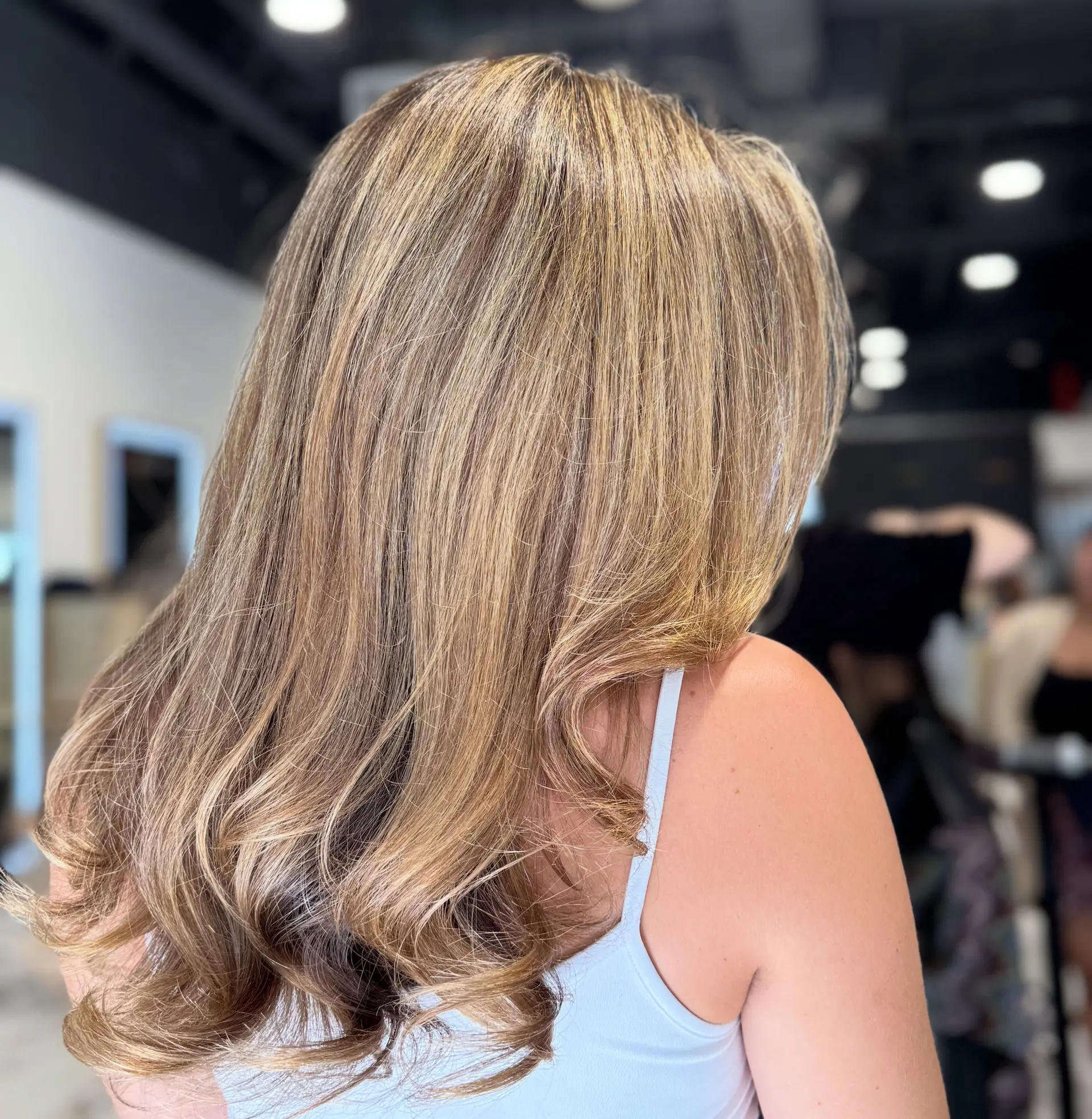 Long honey blonde dimensional highlights blended seamlessly over a light brown base, styled with soft curls at the ends. 1