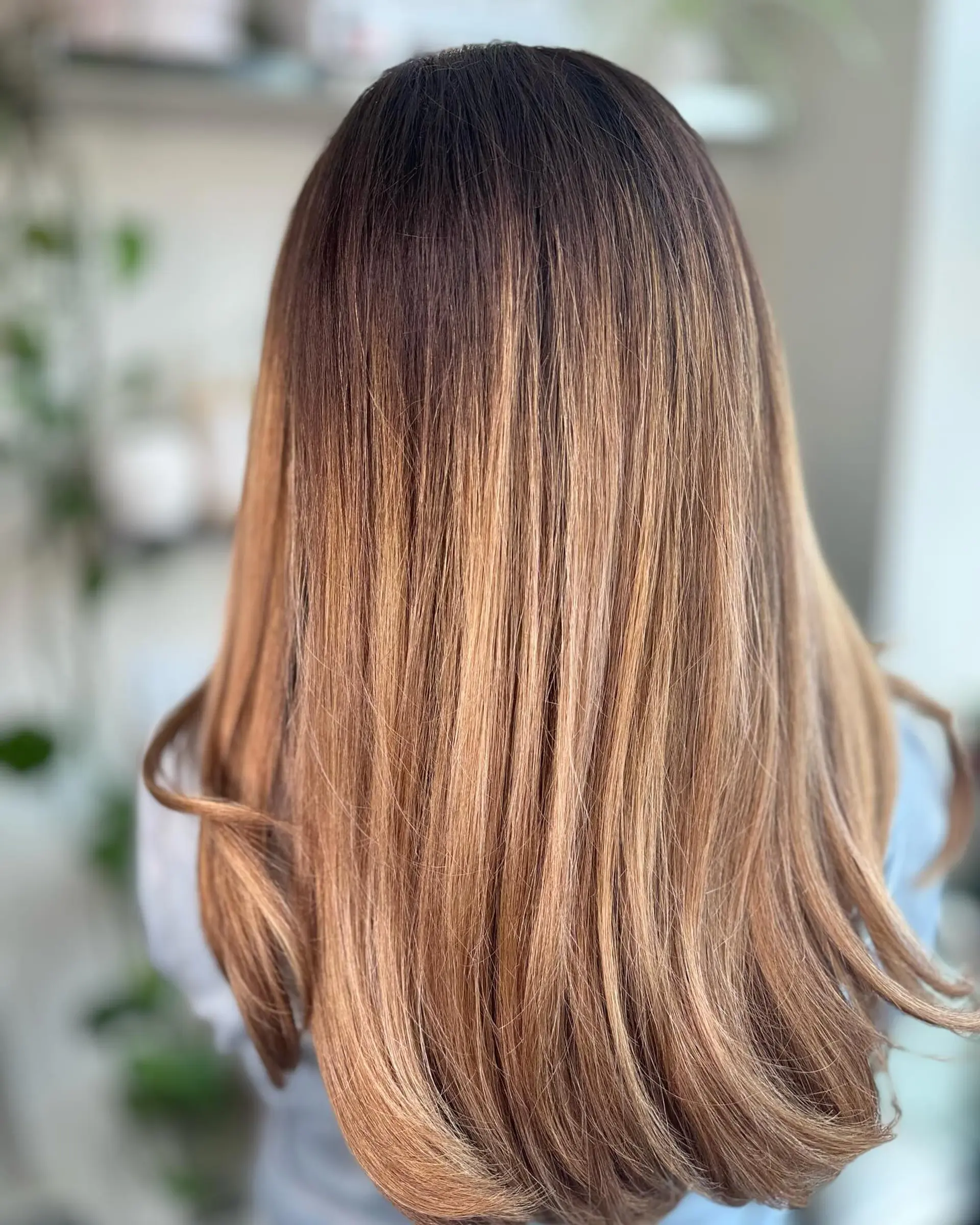 Long, smoothly styled hair featuring a seamless caramel balayage with softly flicked ends. 1