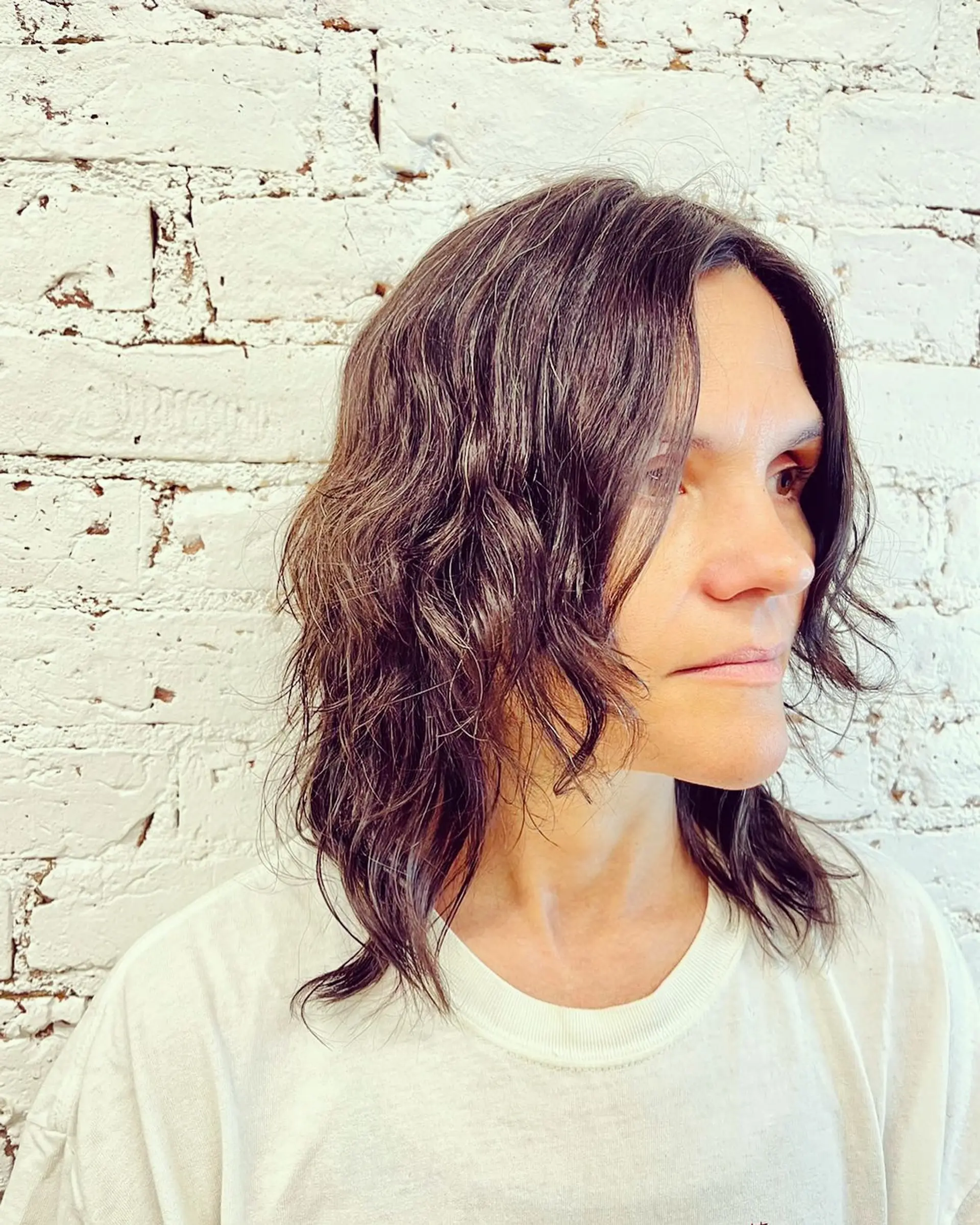 Medium-length layered shag haircut styled with relaxed waves and face-framing texture in dark brown. 1
