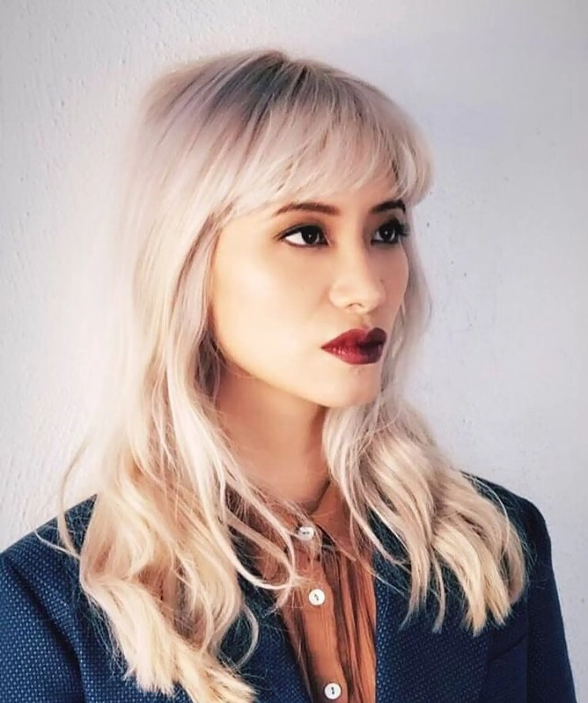 Medium-length platinum blonde hair styled with loose waves and textured straight-across bangs. 1