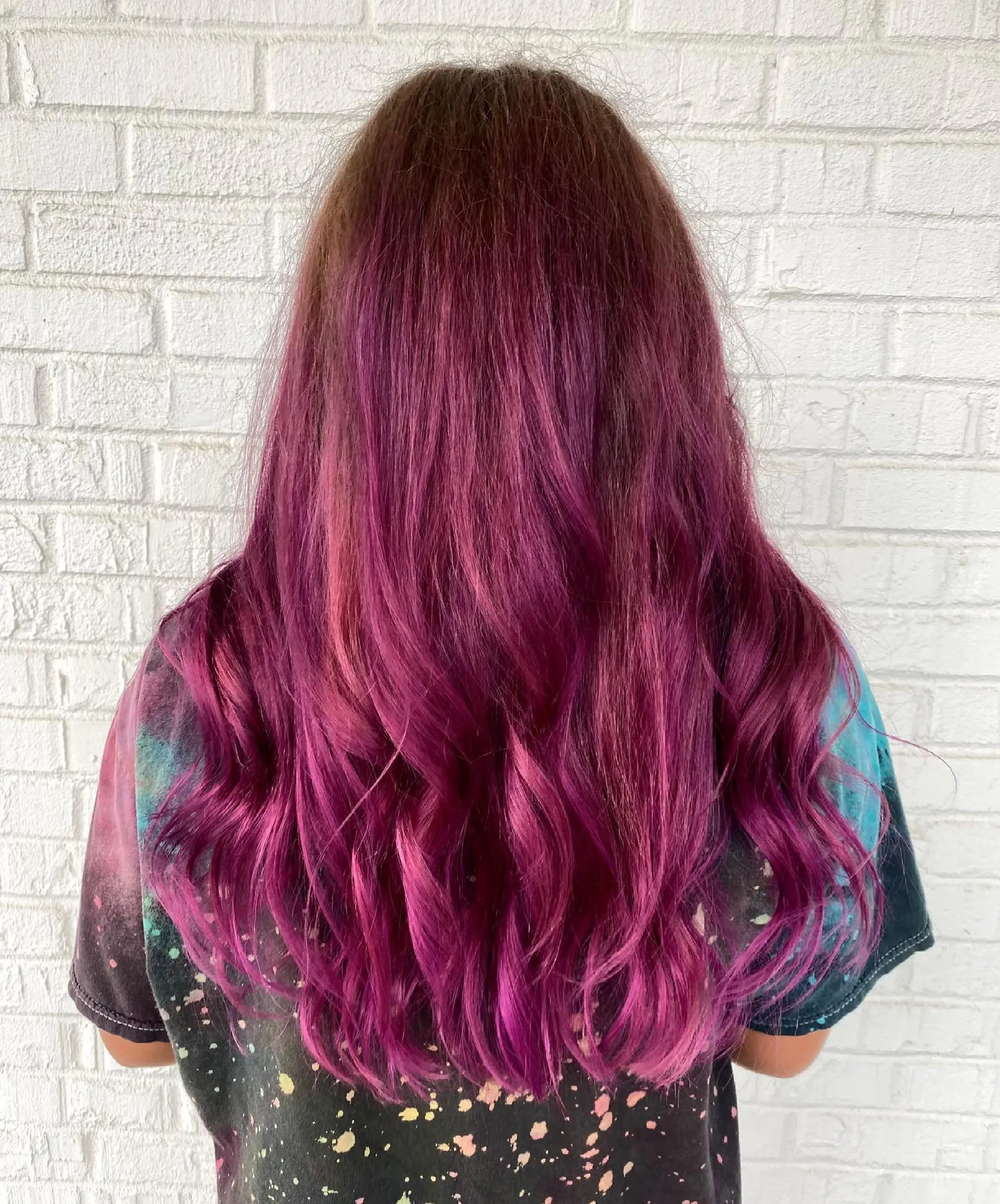 Long hair styled with gentle waves, showcasing a seamless balayage transition from dark roots into vibrant magenta and purple tones. 1