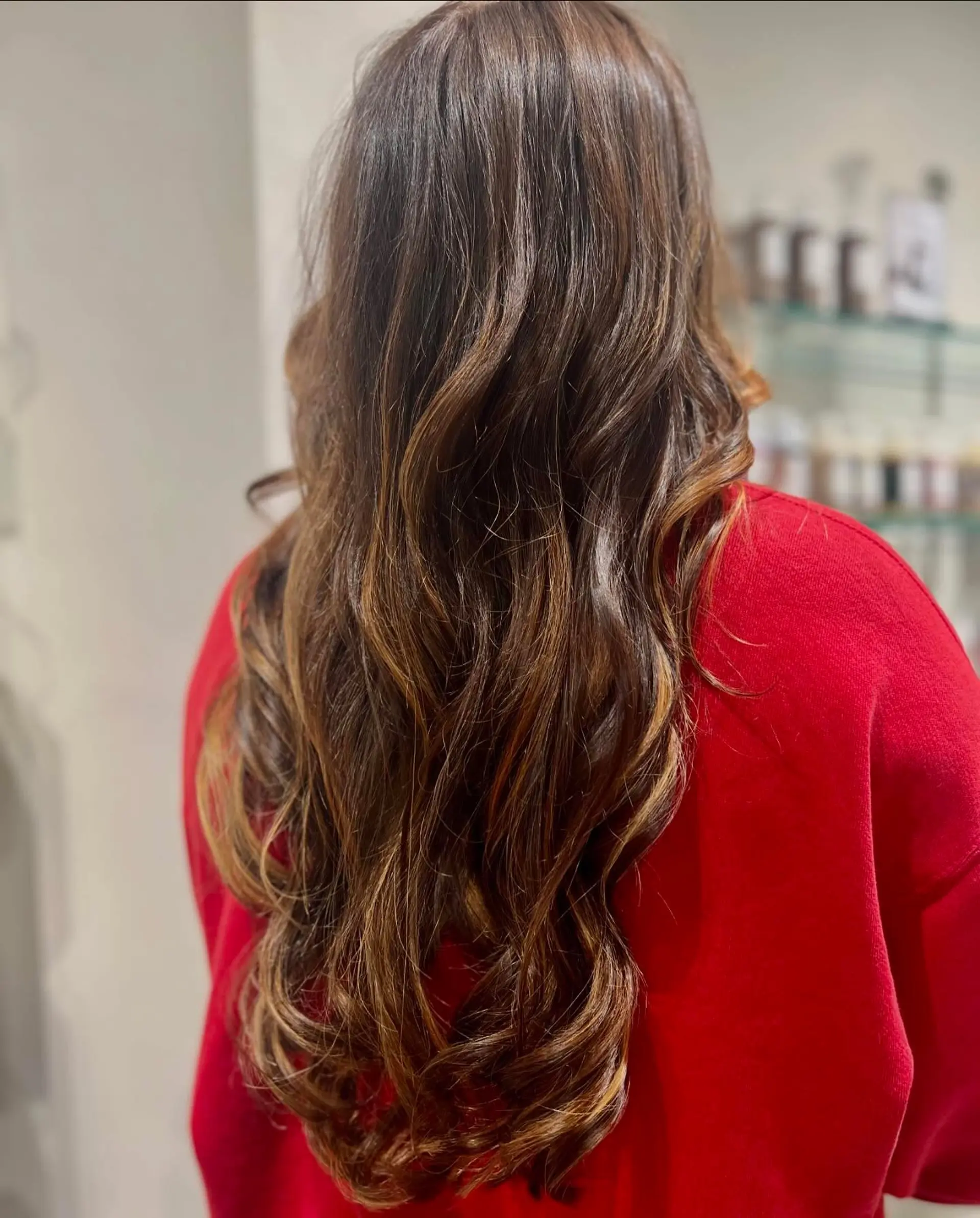 Long dark brown hair enhanced with seamless caramel balayage highlights and styled into soft waves. 1