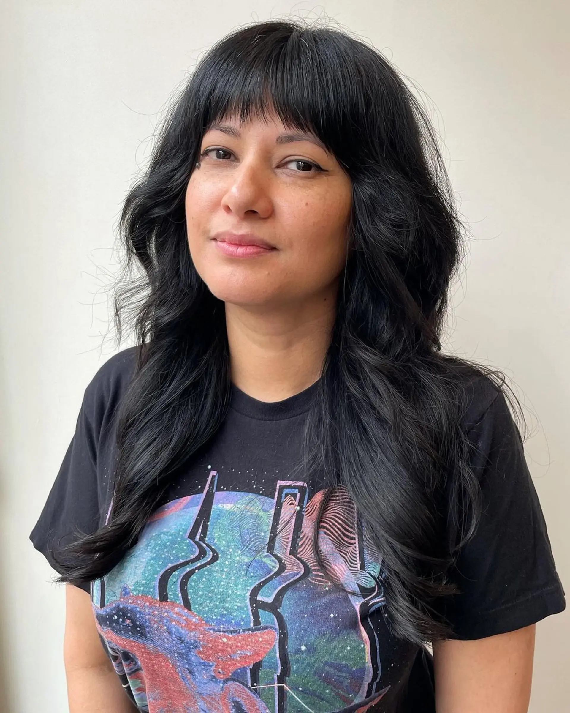 Long, black, wavy hair with a full fringe and face-framing layers, showcasing a glossy, healthy finish and natural waves. 1