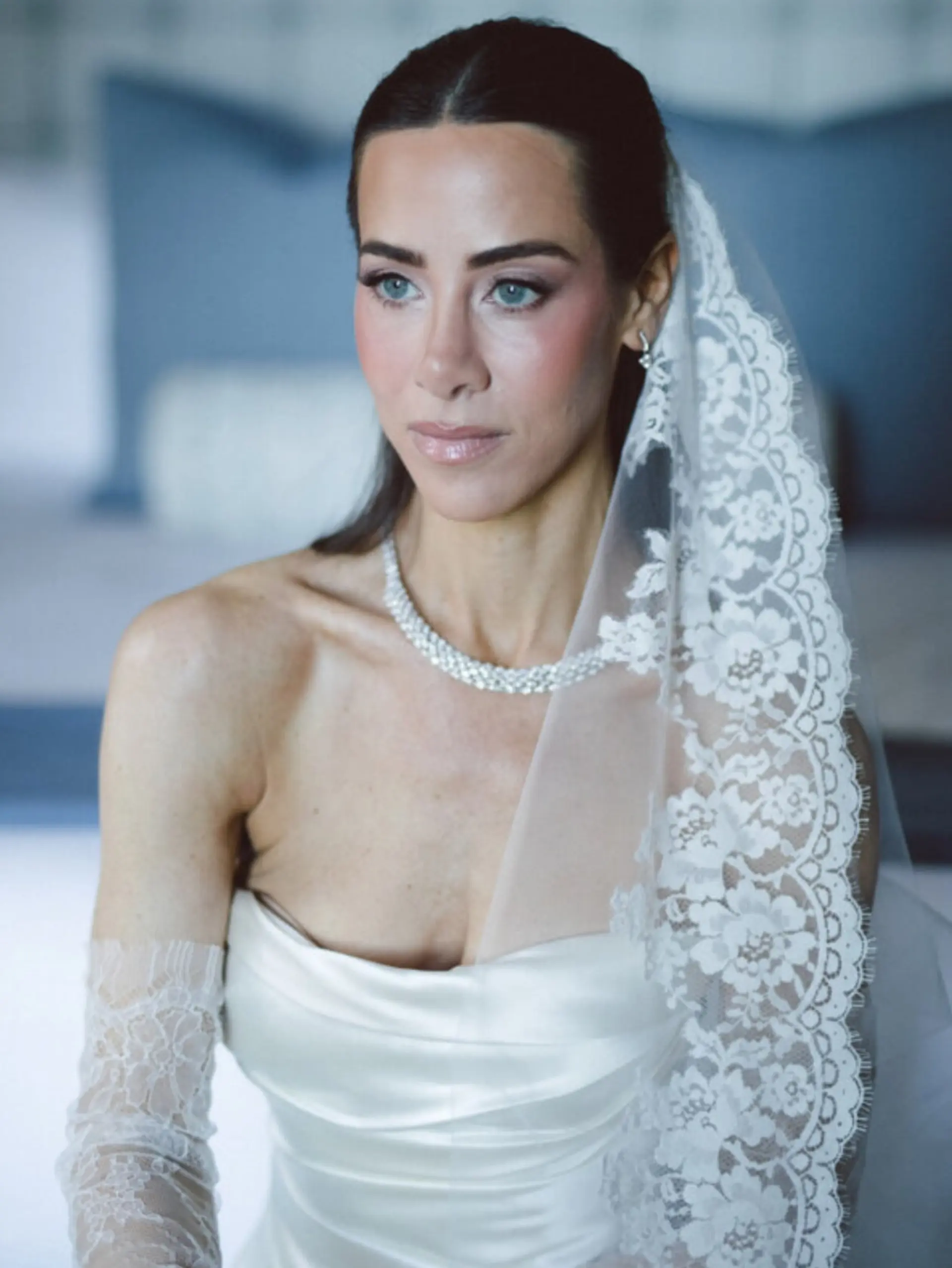 A sleek and sophisticated bridal hairstyle featuring a clean center part and smooth, slicked-back dark hair paired with a lace veil. 1
