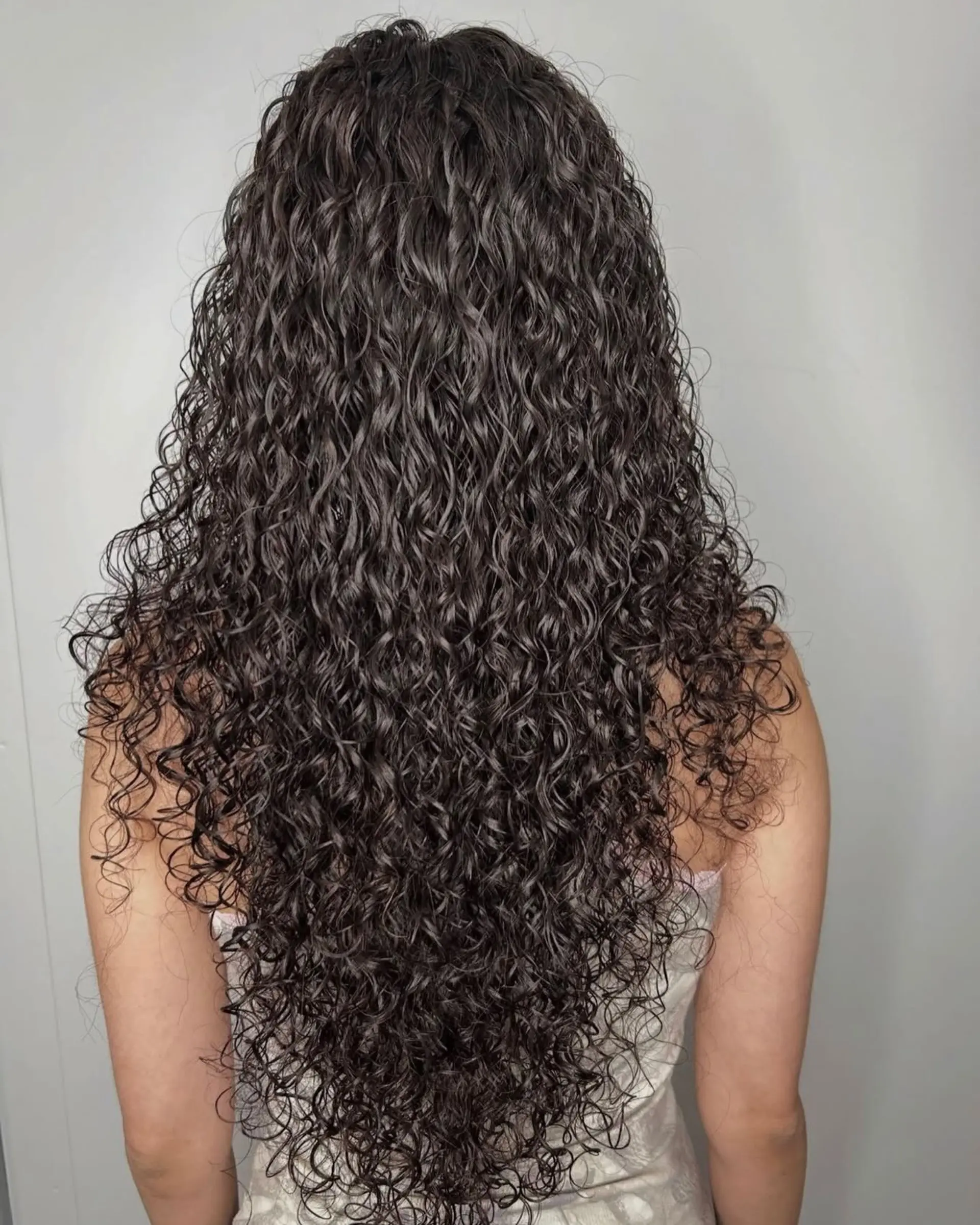 Long, cascading dark hair styled in tight, well-defined spiral perm curls with natural texture and volume. 1