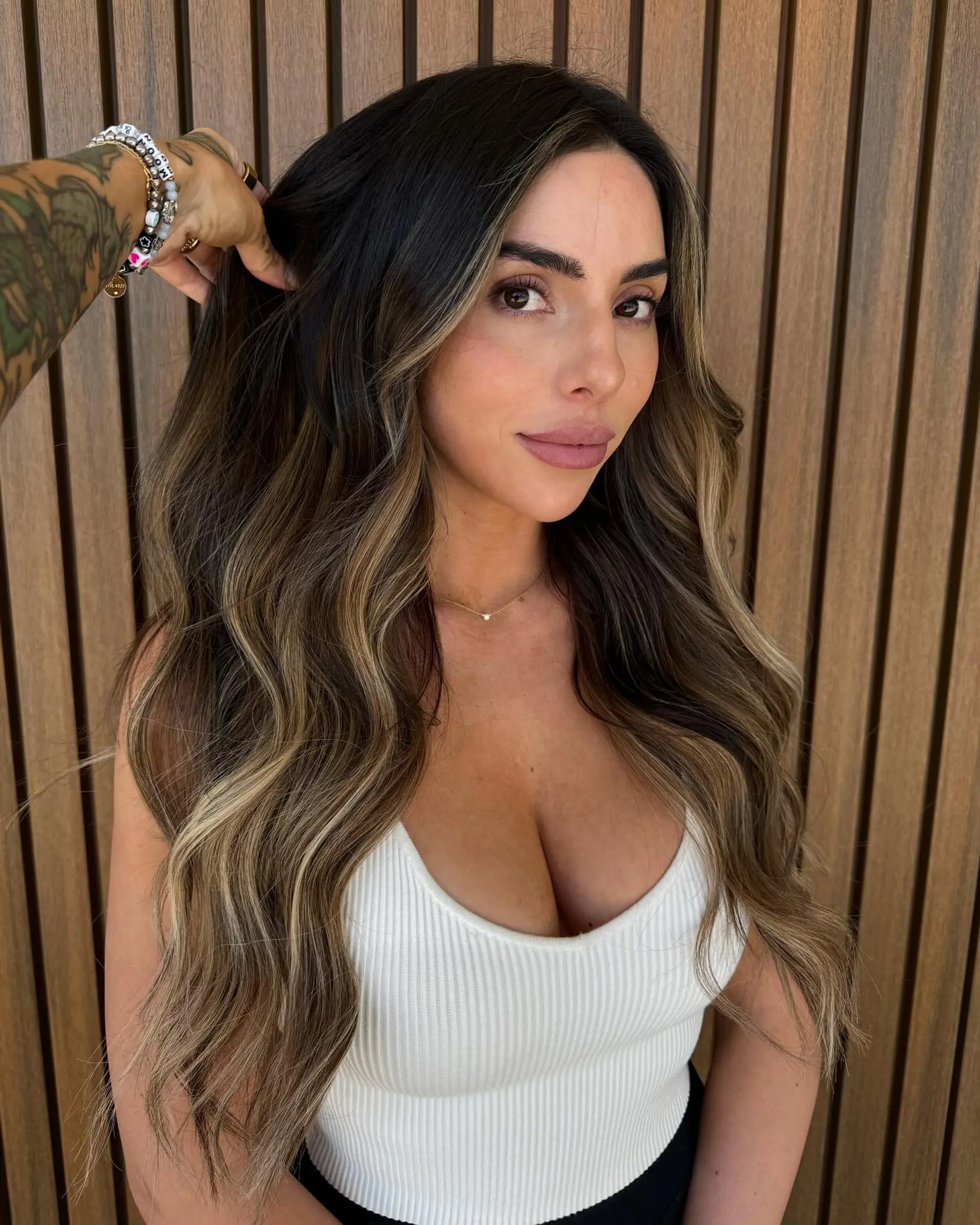 Long dark brunette hair styled in loose, glamorous waves with warm caramel and honey balayage highlights and face-framing dimension. 1
