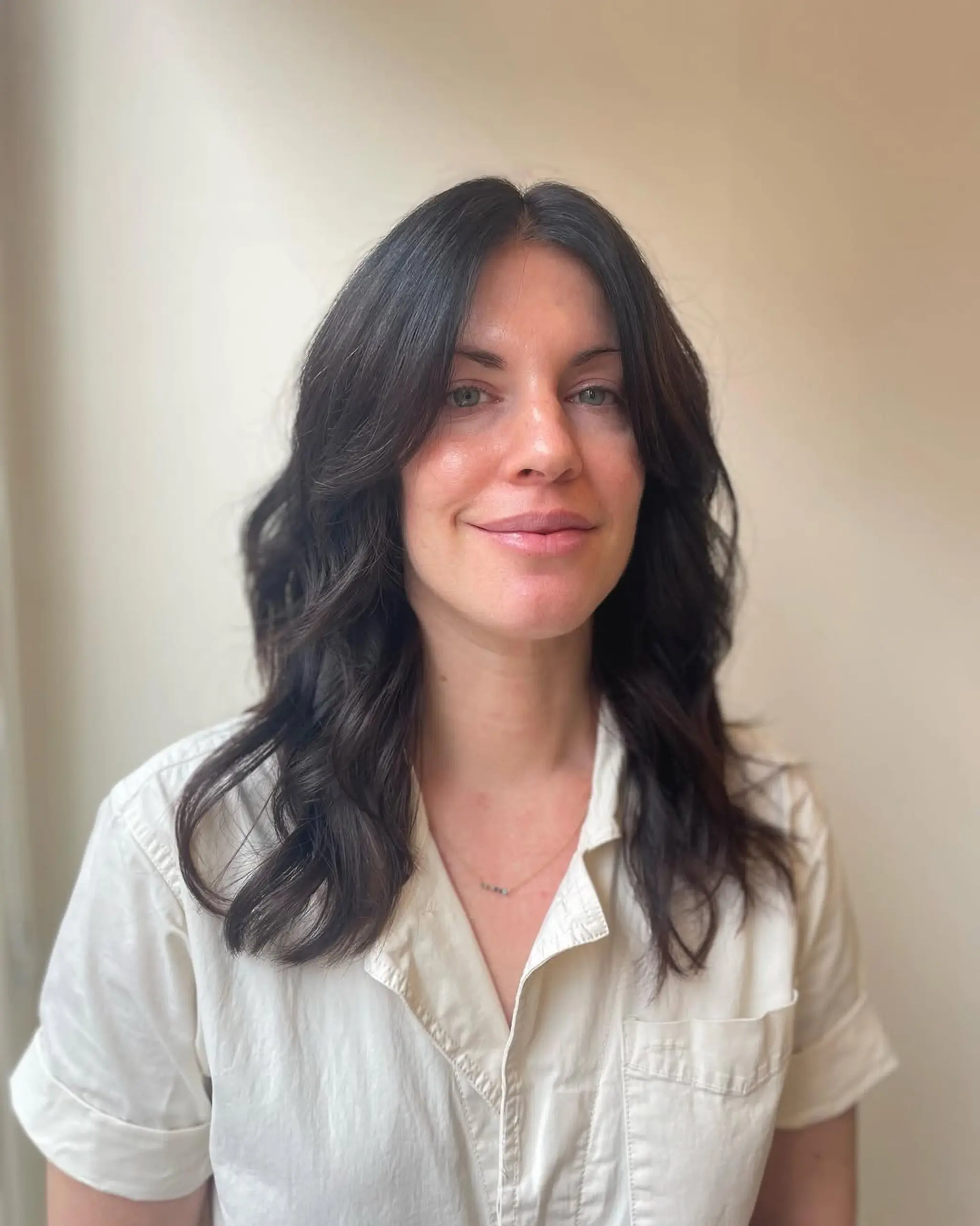 Medium-length dark brown hair with natural waves and layers, featuring a classic side part for a chic and elegant look.