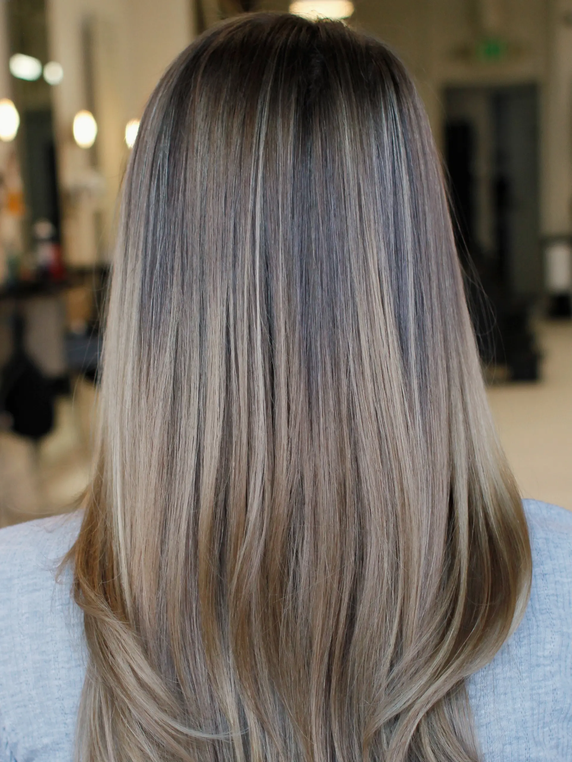 Long, smooth straight hair with a soft bend at the ends, showcasing cool-toned milky latte blonde highlights seamlessly blended into a neutral brown base. 1