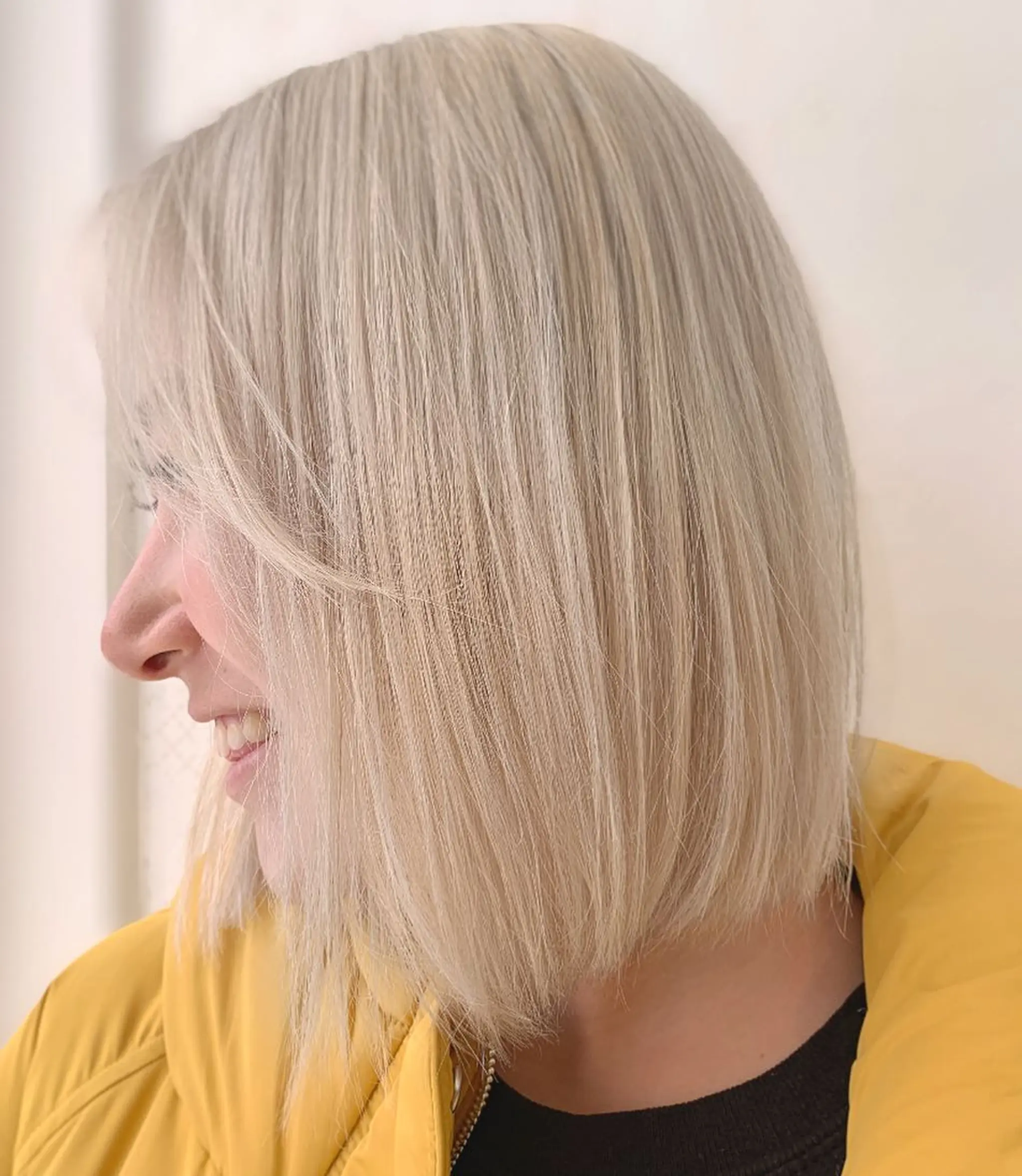 A sleek, straight, medium-length bob with a blunt edge and a side part, colored in platinum blonde.