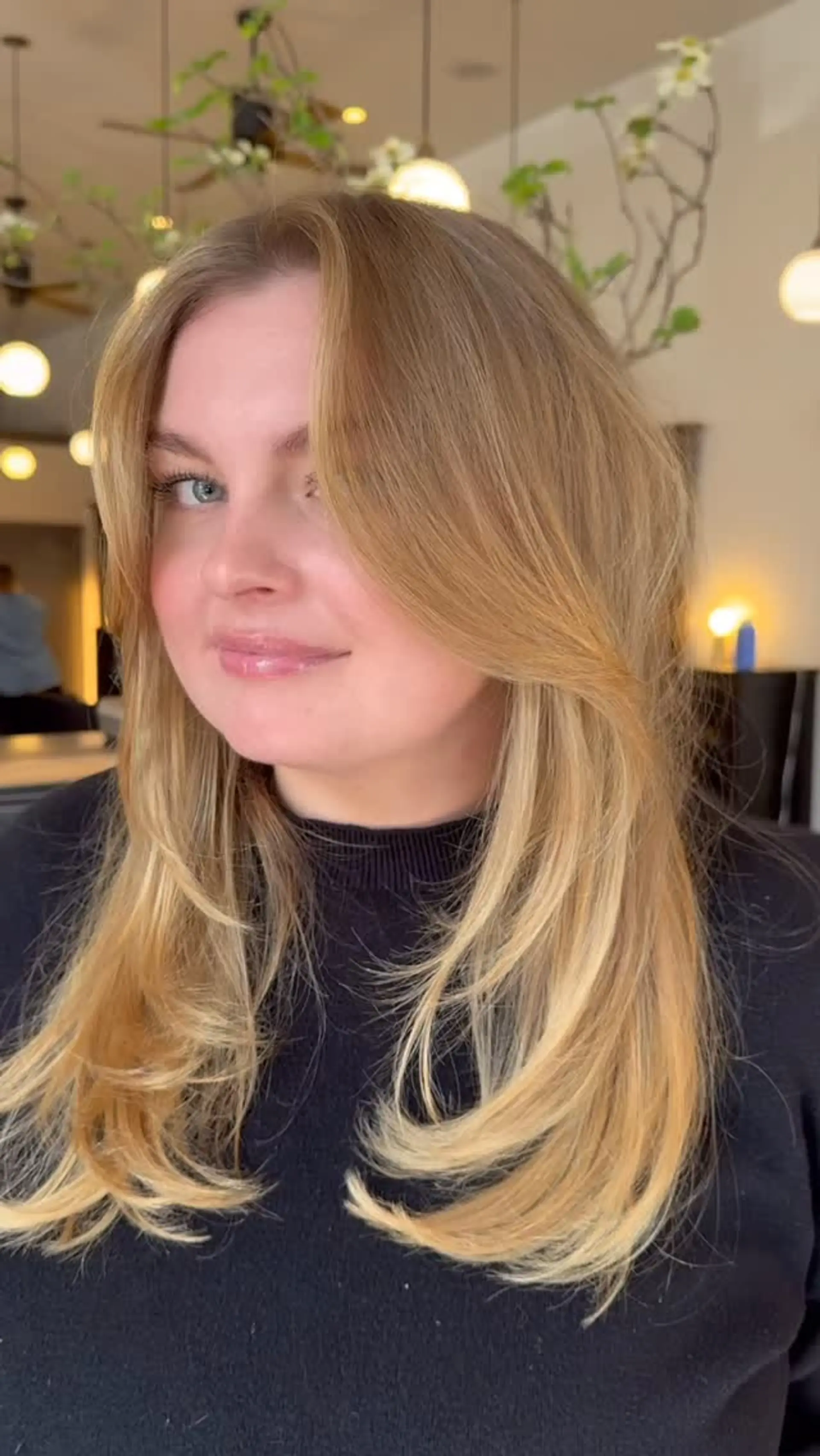 Long warm golden blonde hair styled in voluminous, bouncy layers with face-framing curtain bangs. 1