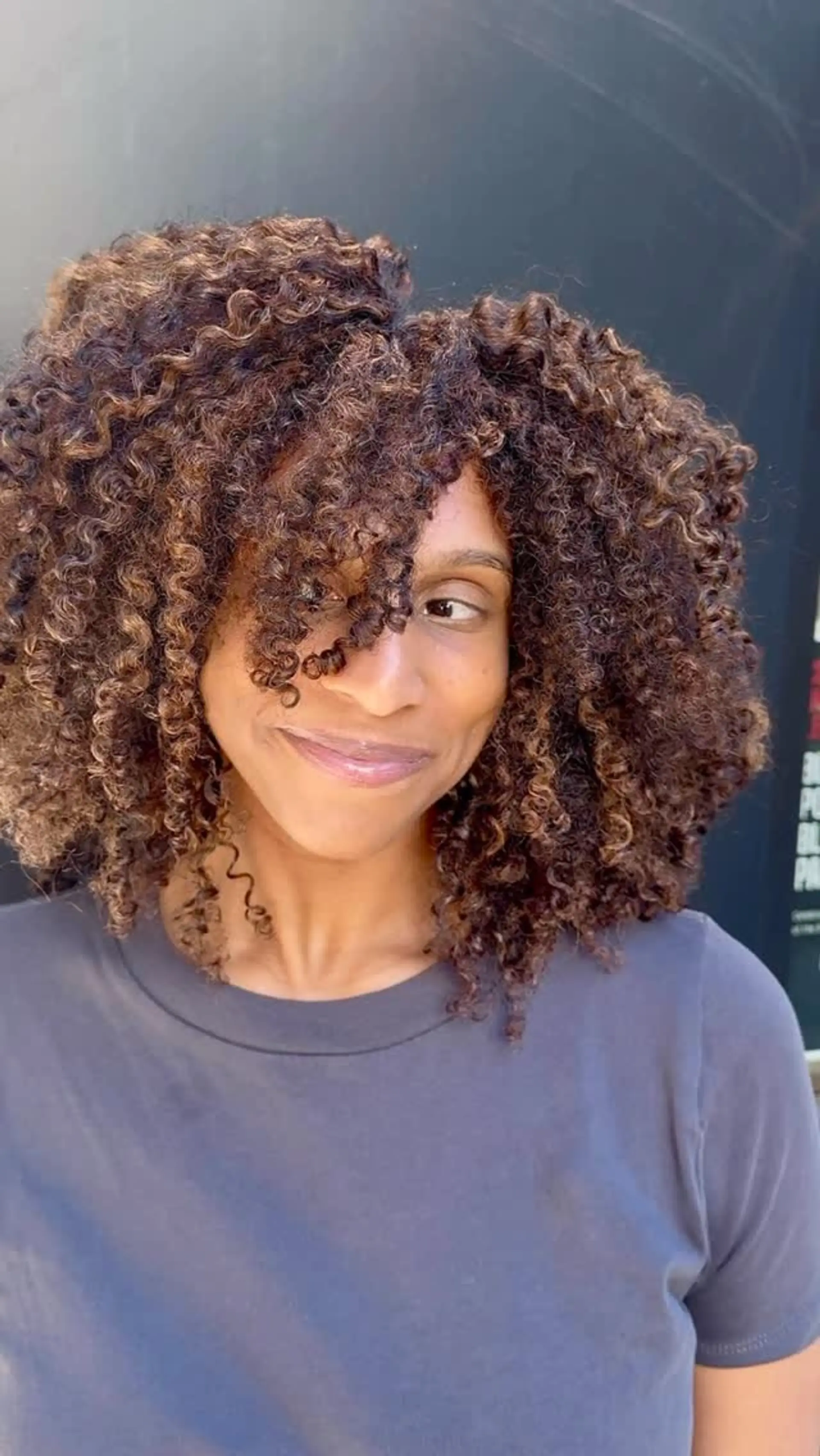 Shoulder-length defined curls cut with rounded layering, face-framing fringe, and warm dimensional balayage highlights. 1