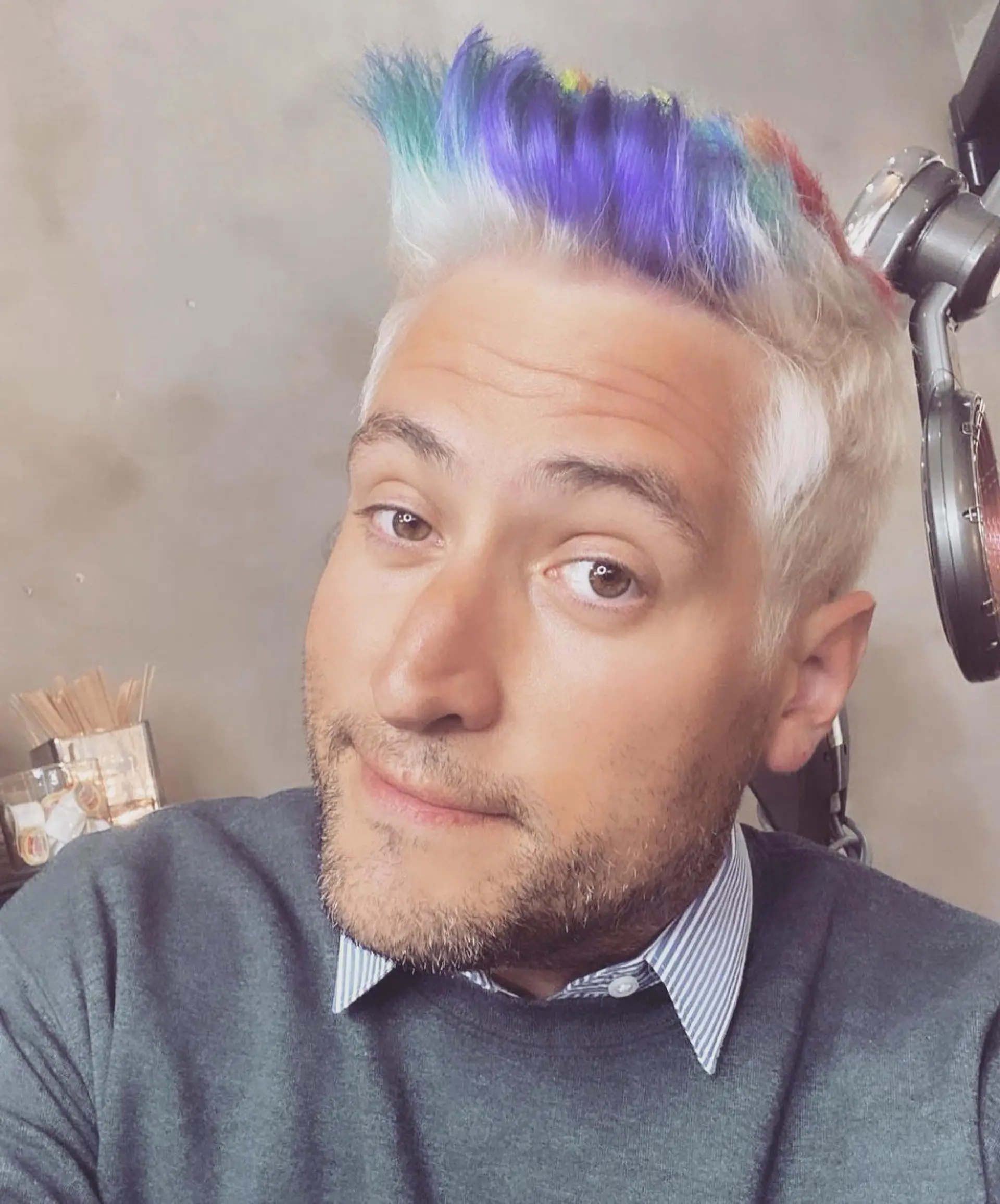 A short platinum blonde cut styled upward into a textured quiff with vivid rainbow-colored tips. 1
