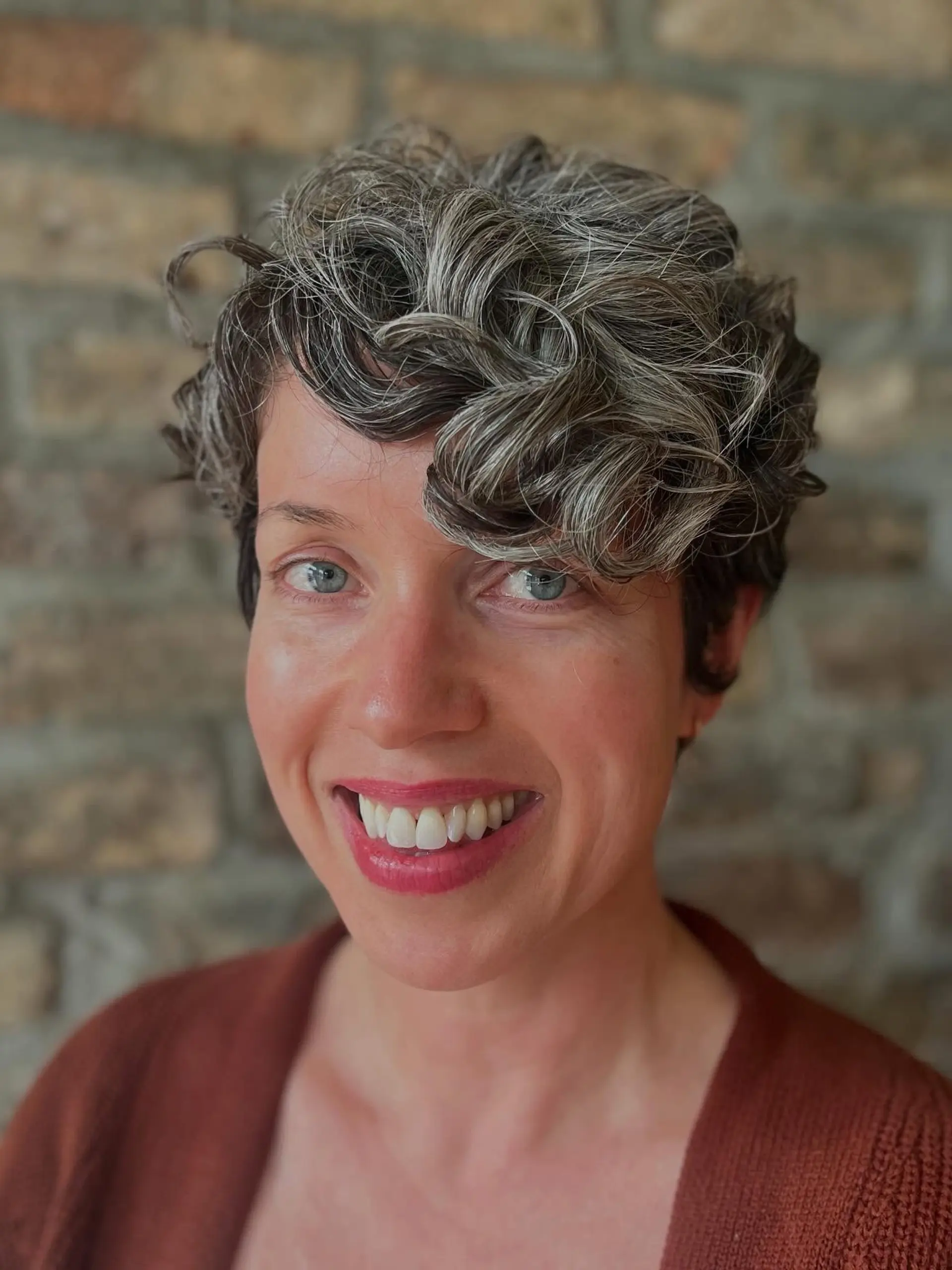A short, curly pixie cut with textured layers and natural silver highlights. 1