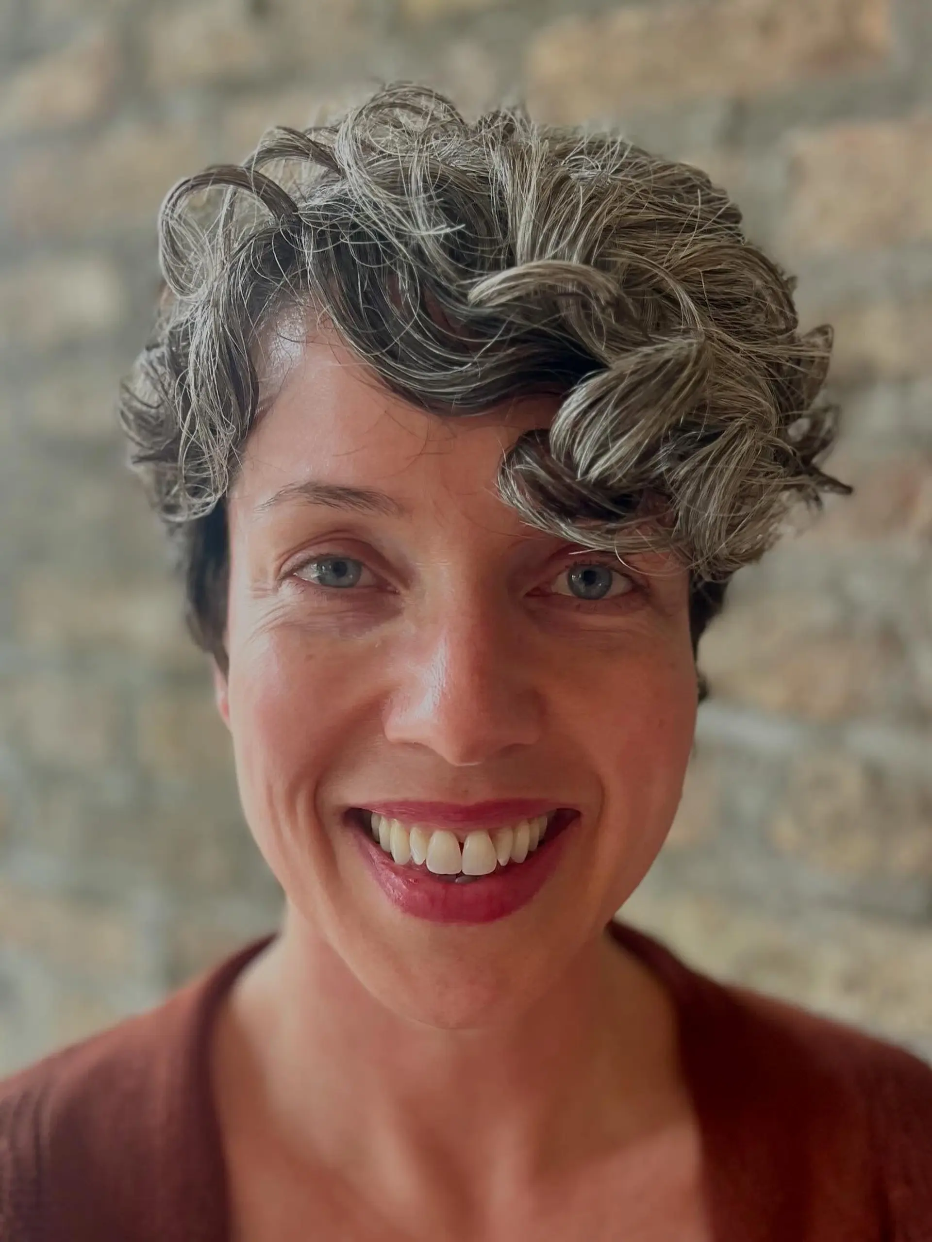 A short, curly pixie cut with textured layers and natural silver highlights. 2