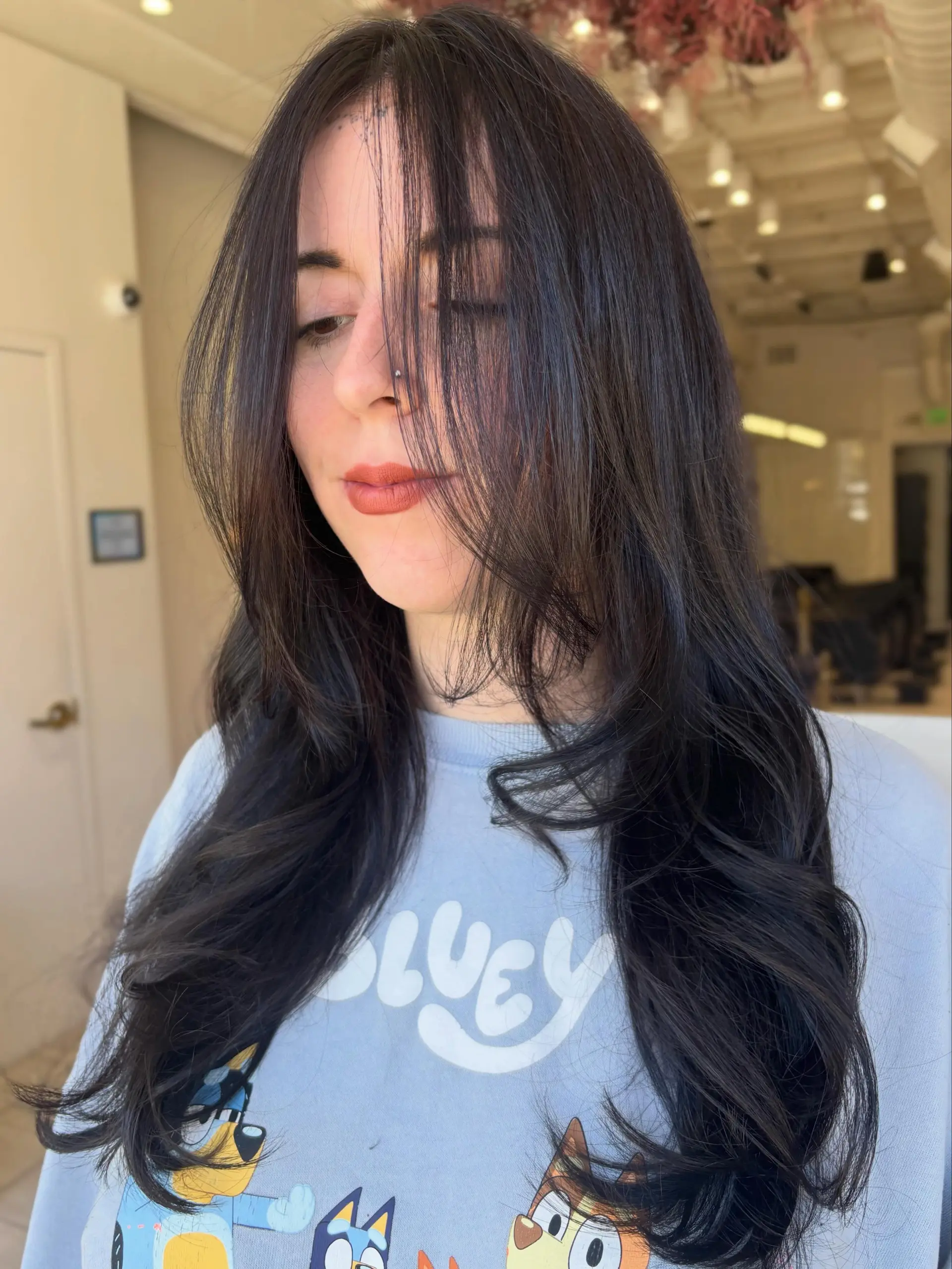 Glossy, deep chocolate brown hair cut into long layers with wispy face-framing fringe and styled in soft, outward-curling waves at the ends. 1