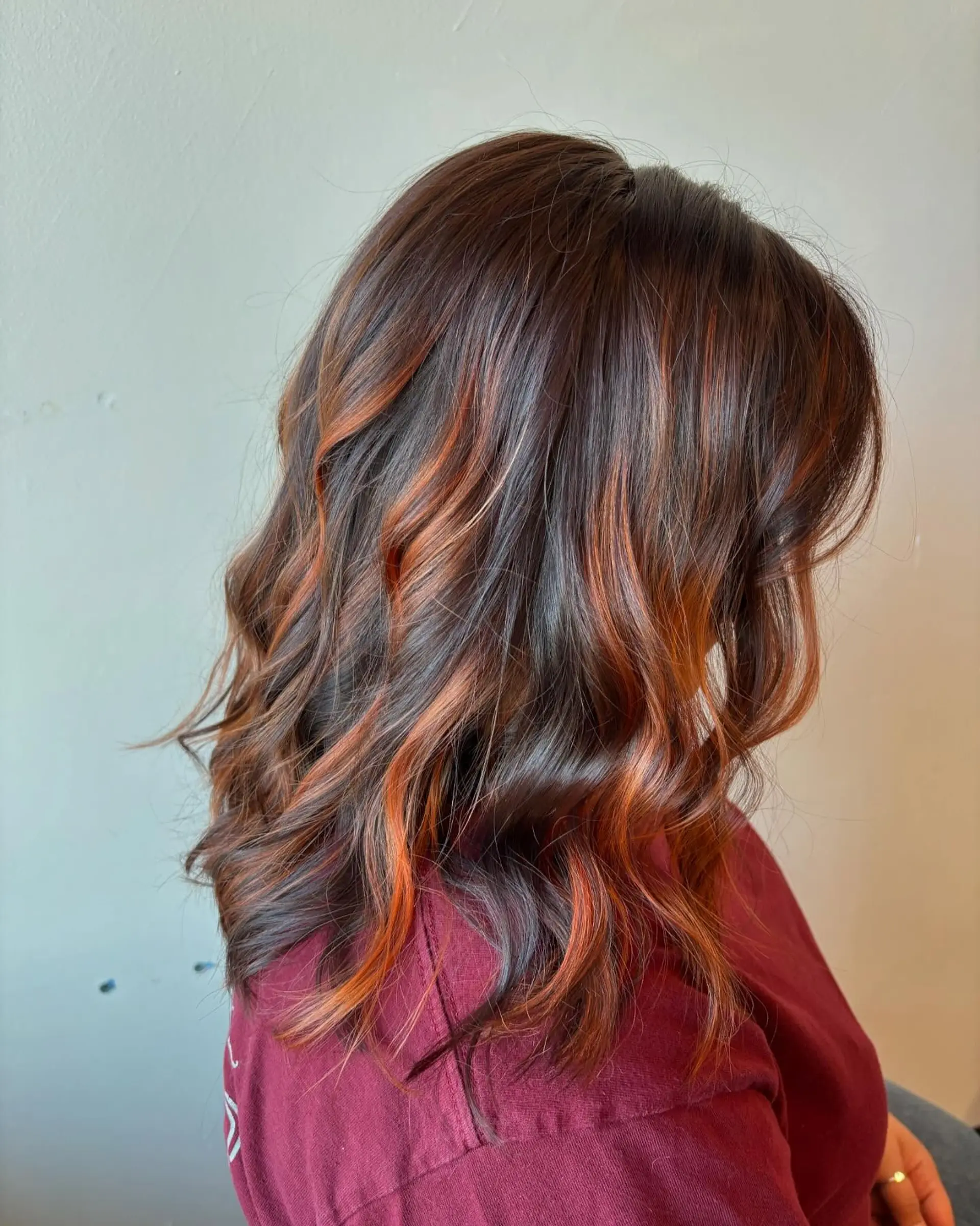 Medium-length dark brown hair featuring hand-painted copper balayage highlights styled in soft, dimensional waves. 1