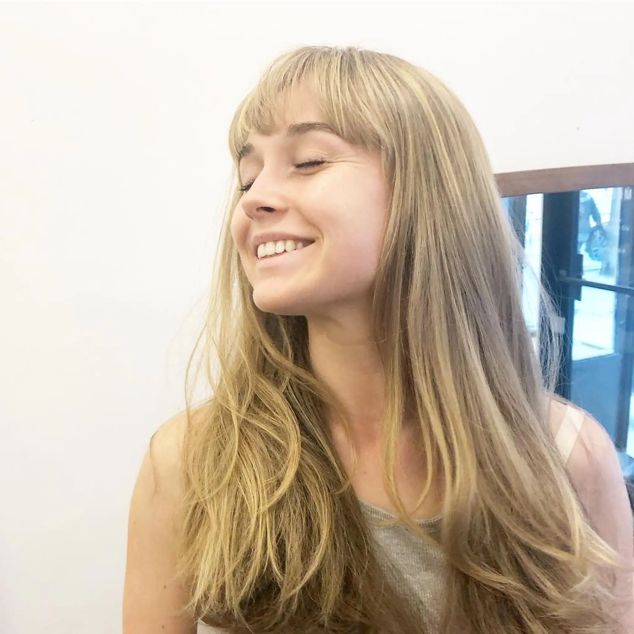 Long, straight, blonde hair with golden highlights, featuring long layers and soft bangs. Styled with Dyson hairdryer.